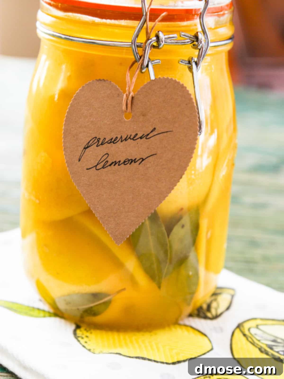 A tall clamp jar filled with preserved lemons, bay leaves, and a brown paper tag.