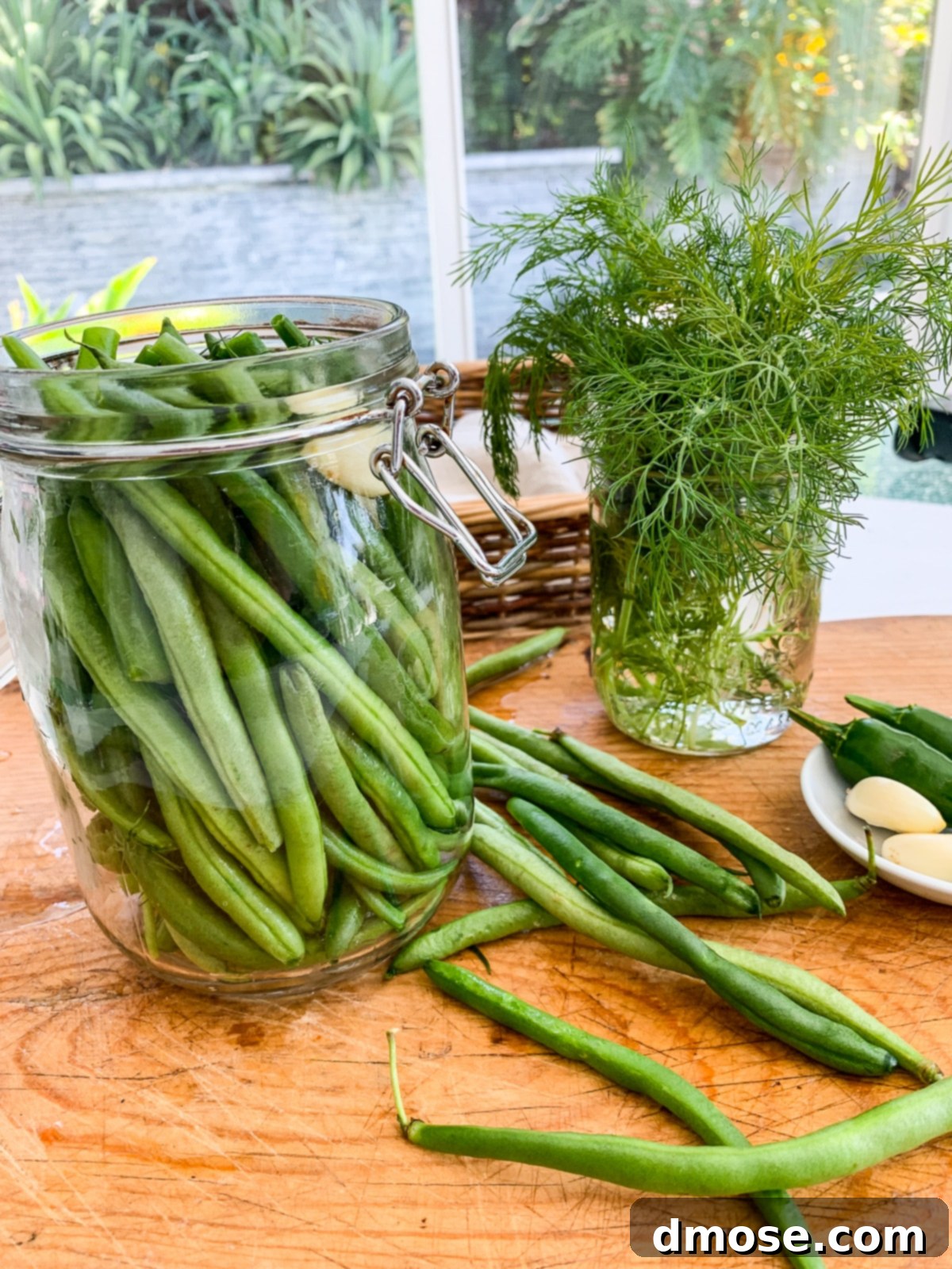A person arranging green beans and spices on a cutting board, preparing them for pickling.