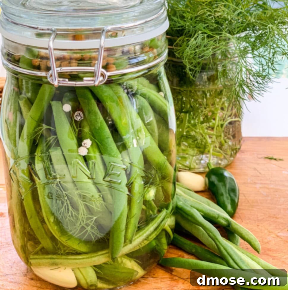 A clear glass jar filled with pickled green beans on a cutting board.