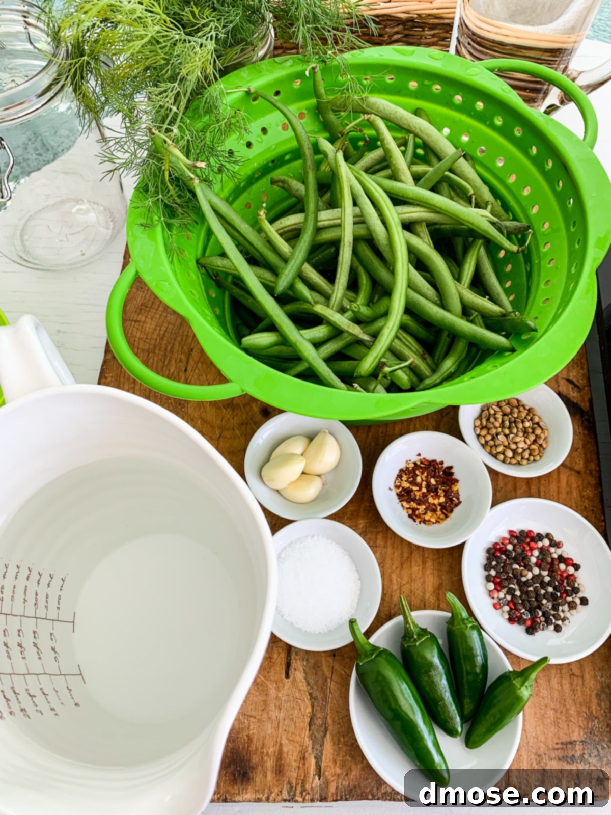 A collection of ingredients for making pickled green beans on a wooden cutting board.