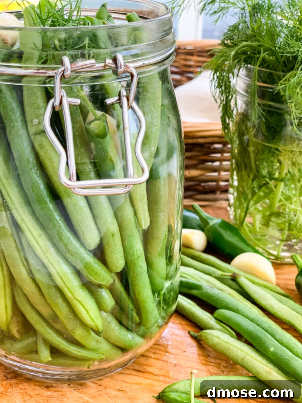 A person loading trimmed green beans into a clamp-top jar with aromatics.