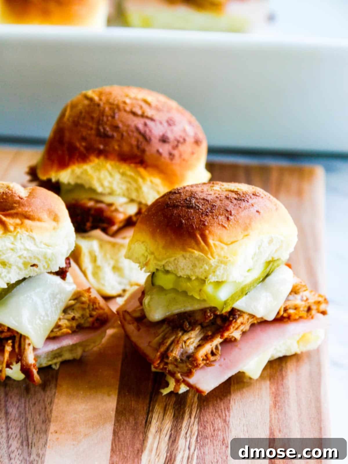 Three pulled pork sliders arranged neatly on a cutting board, garnished with fresh herbs, showcasing their golden-brown tops and delicious fillings.