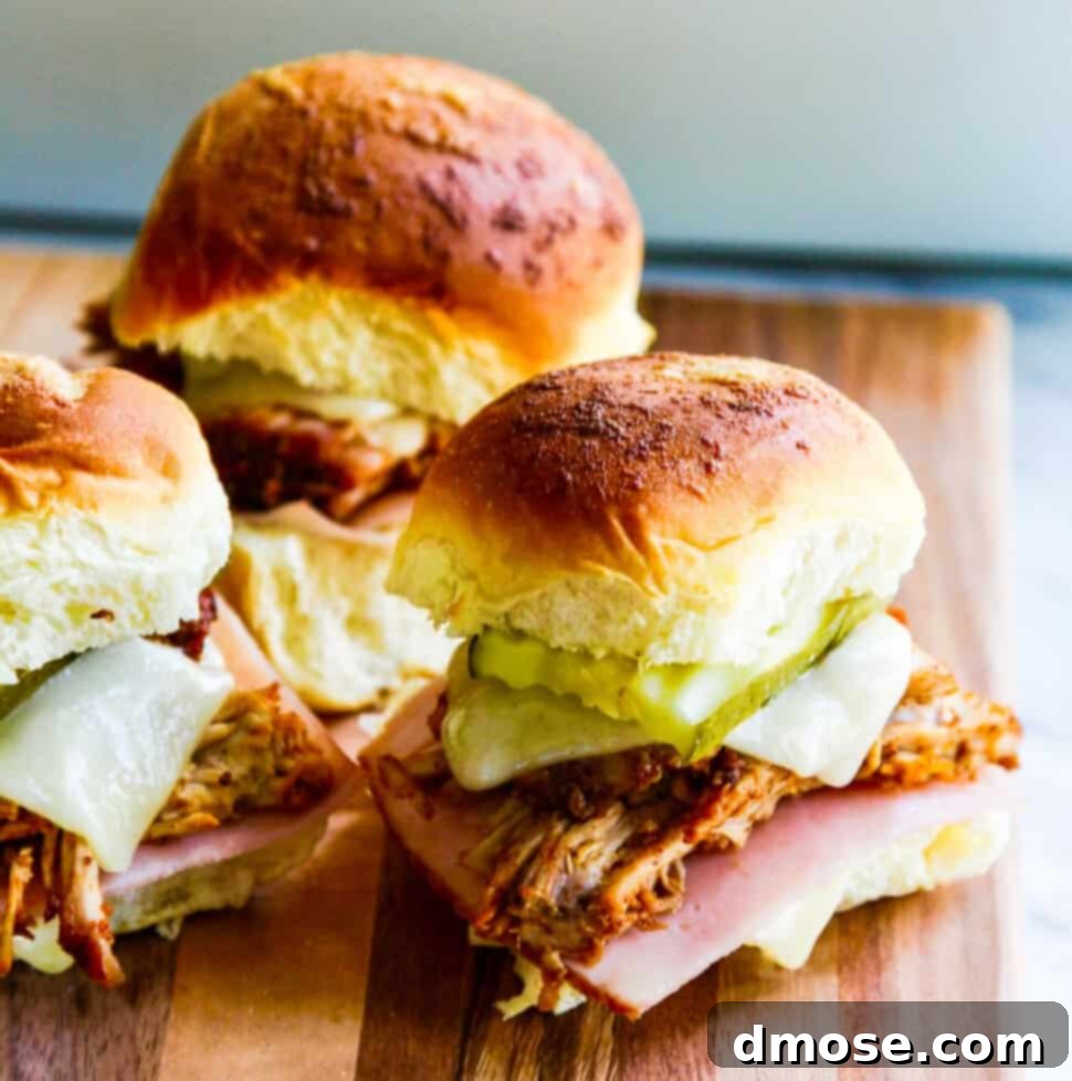 Three pulled pork sandwiches on Hawaiian buns with pickles, cheese and ham on a cutting board, perfectly assembled and ready to eat.