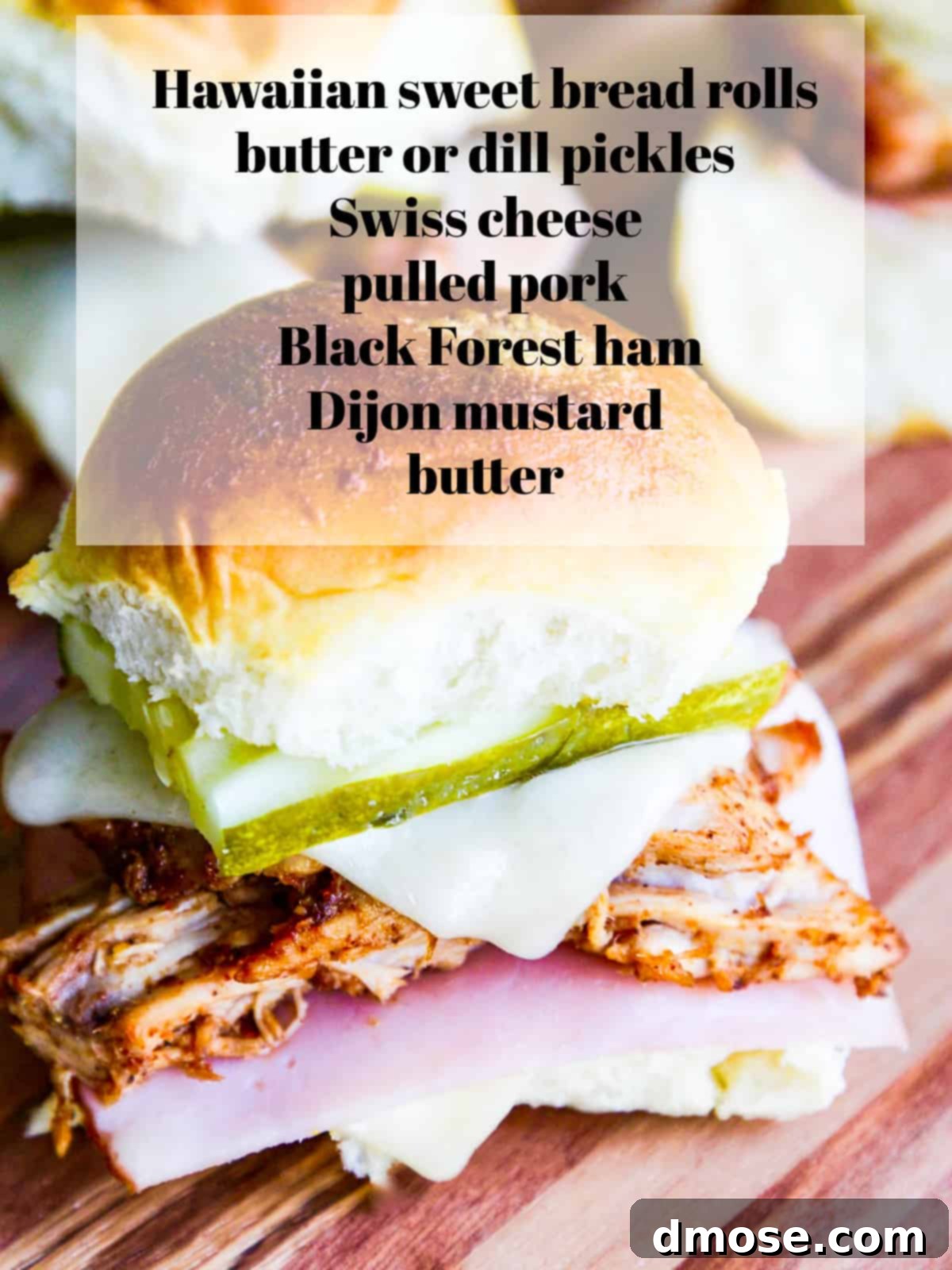 Ingredients for pulled pork sliders laid out on a wooden surface: Hawaiian rolls, sliced ham, a bowl of pulled pork, Swiss cheese, dill pickles, butter, and Dijon mustard.