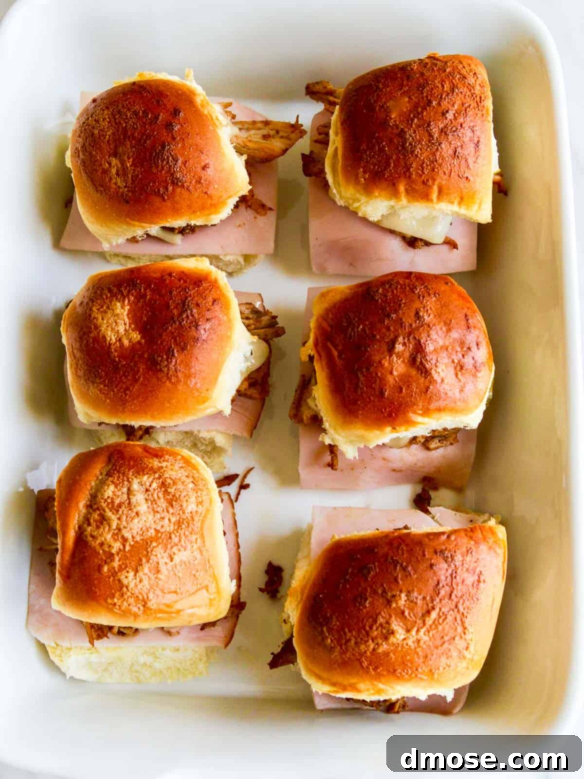 A white rectangular baking dish filled with numerous freshly baked pulled pork sliders, ready for serving at a gathering.