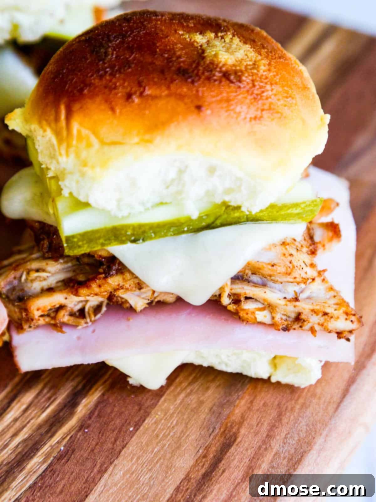A single baked pulled pork slider on a wooden cutting board, cut in half to clearly display the melted Swiss cheese, tender pulled pork, and vibrant dill pickles.