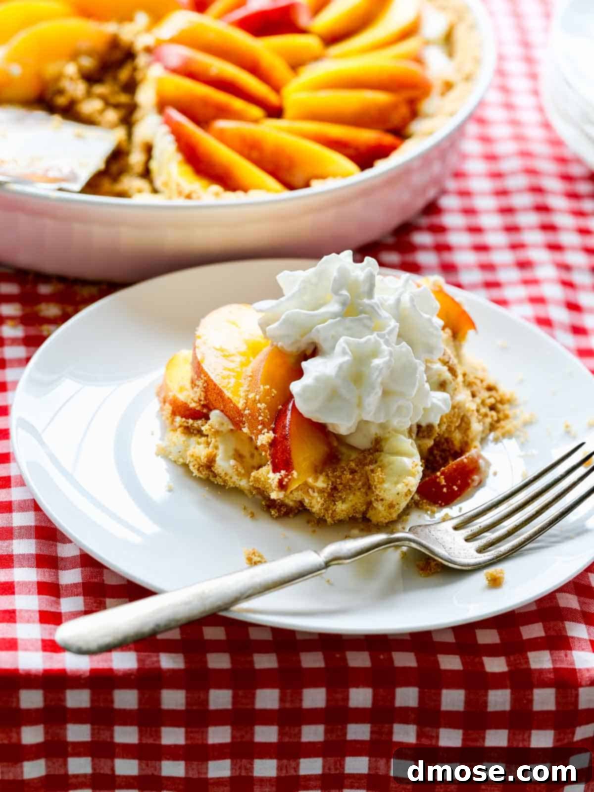 A beautiful slice of no-bake peach cheesecake pie on a white plate, showcasing the layers of graham cracker crust, creamy filling, and fresh peach slices.