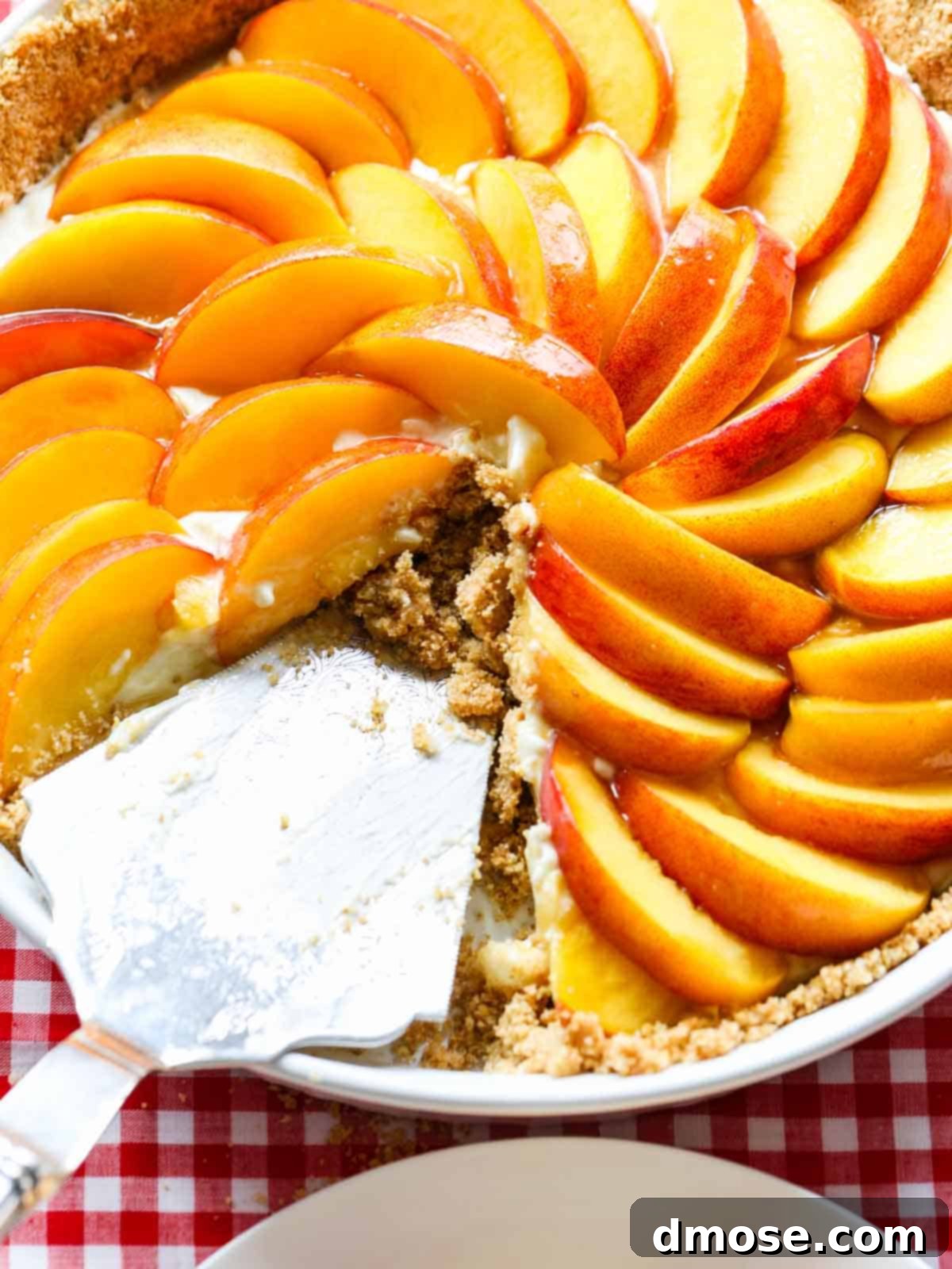 A whole no-bake peach cheesecake pie with a slice removed, revealing the creamy texture and layers of crust and fruit.