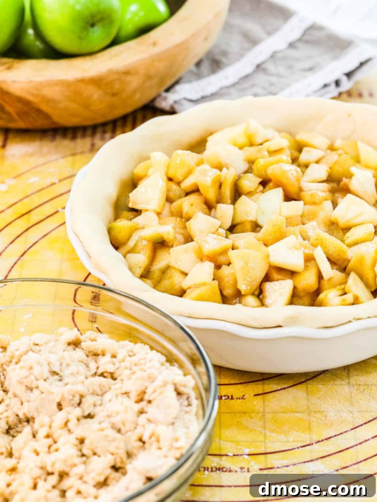 A white pie dish with pie dough filled with apple pie filling ready to bake.