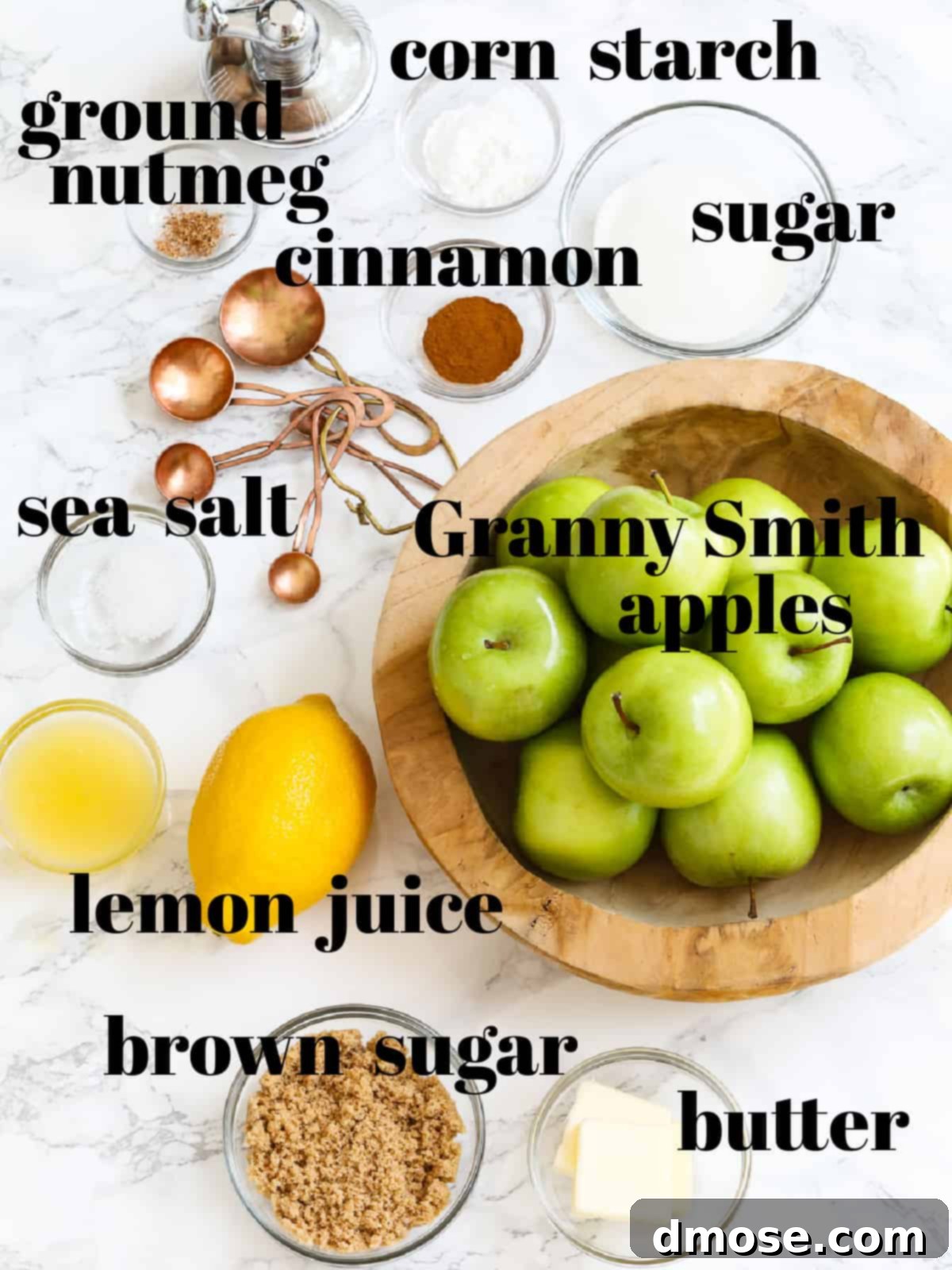 A selection of ingredients for homemade apple pie filling including Granny Smith apples, butter, sugars, spices, and lemon.