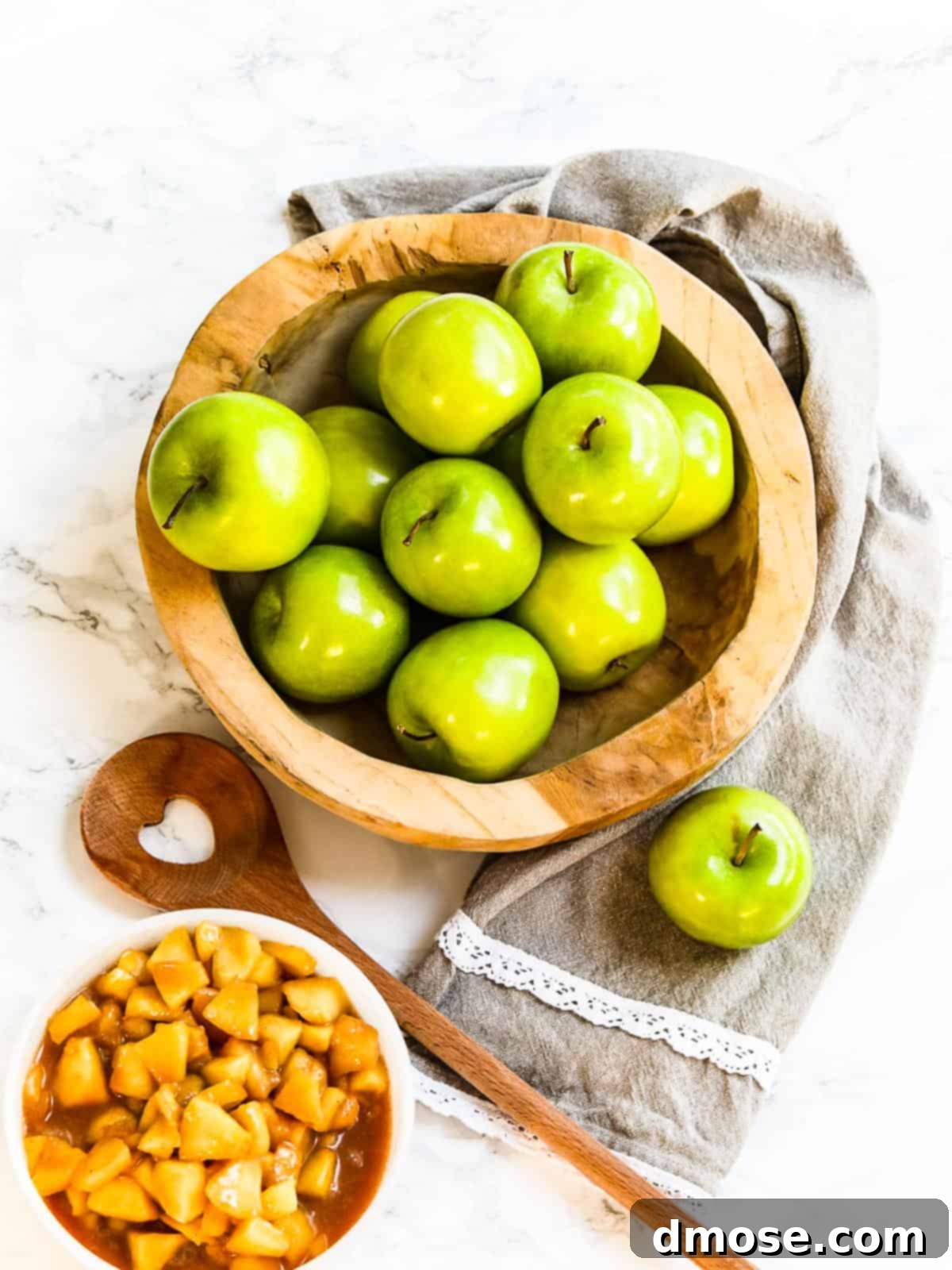 A small bowl of cooked apple pie filling with whole green apples in the background.