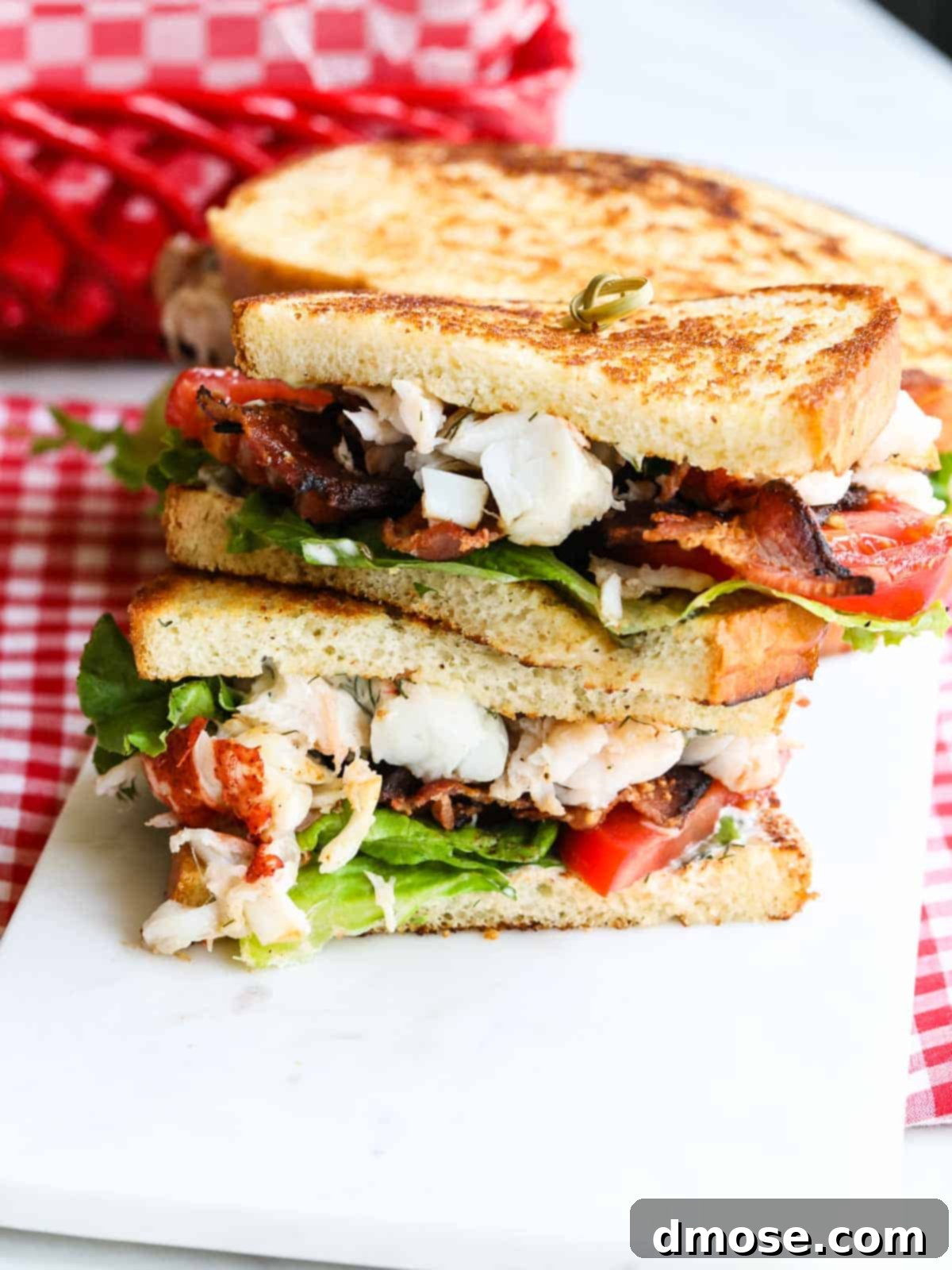 A perfectly assembled and sliced BLT lobster sandwich, presented invitingly to highlight its gourmet ingredients and deliciousness.