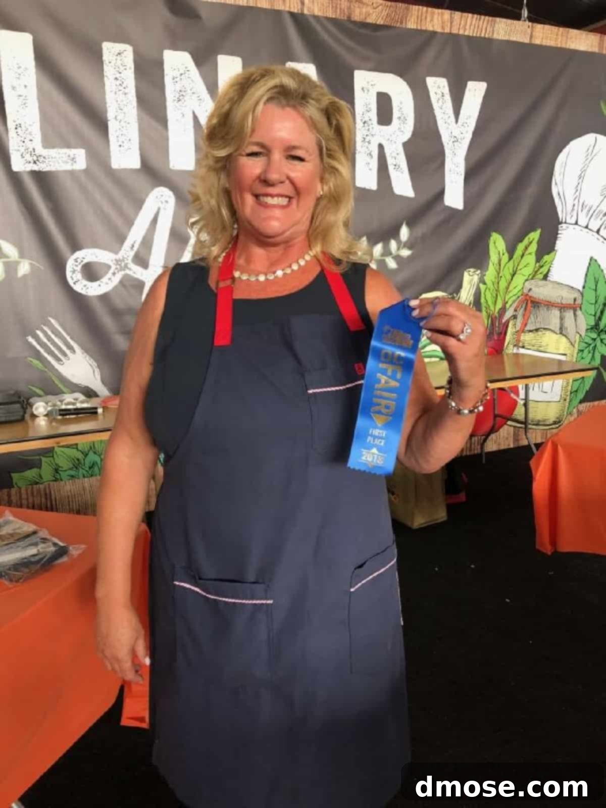 Lisa Hatfield, smiling proudly, holding her blue ribbon and the award-winning Lobster BLT Sandwich, a testament to her culinary achievement at the Orange County Fair.