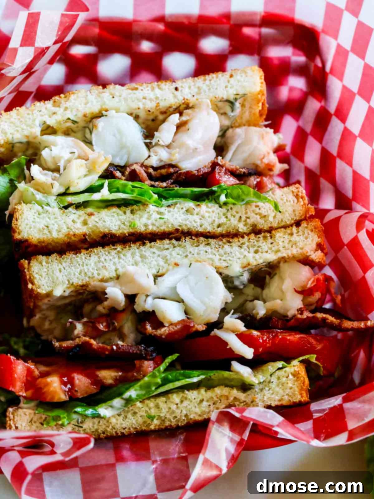 A delicious BLT lobster sandwich, beautifully arranged in a classic red and white check paper-lined food basket, invitingly ready to be enjoyed.