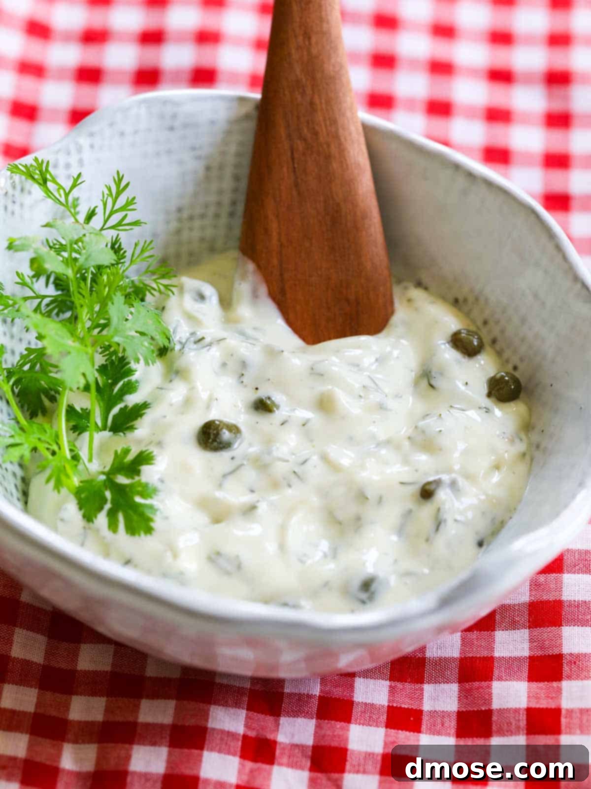 A pristine white bowl filled with the vibrant green dill-caper aioli, garnished with fresh dill sprigs, ready to be used for the lobster BLT sandwich.