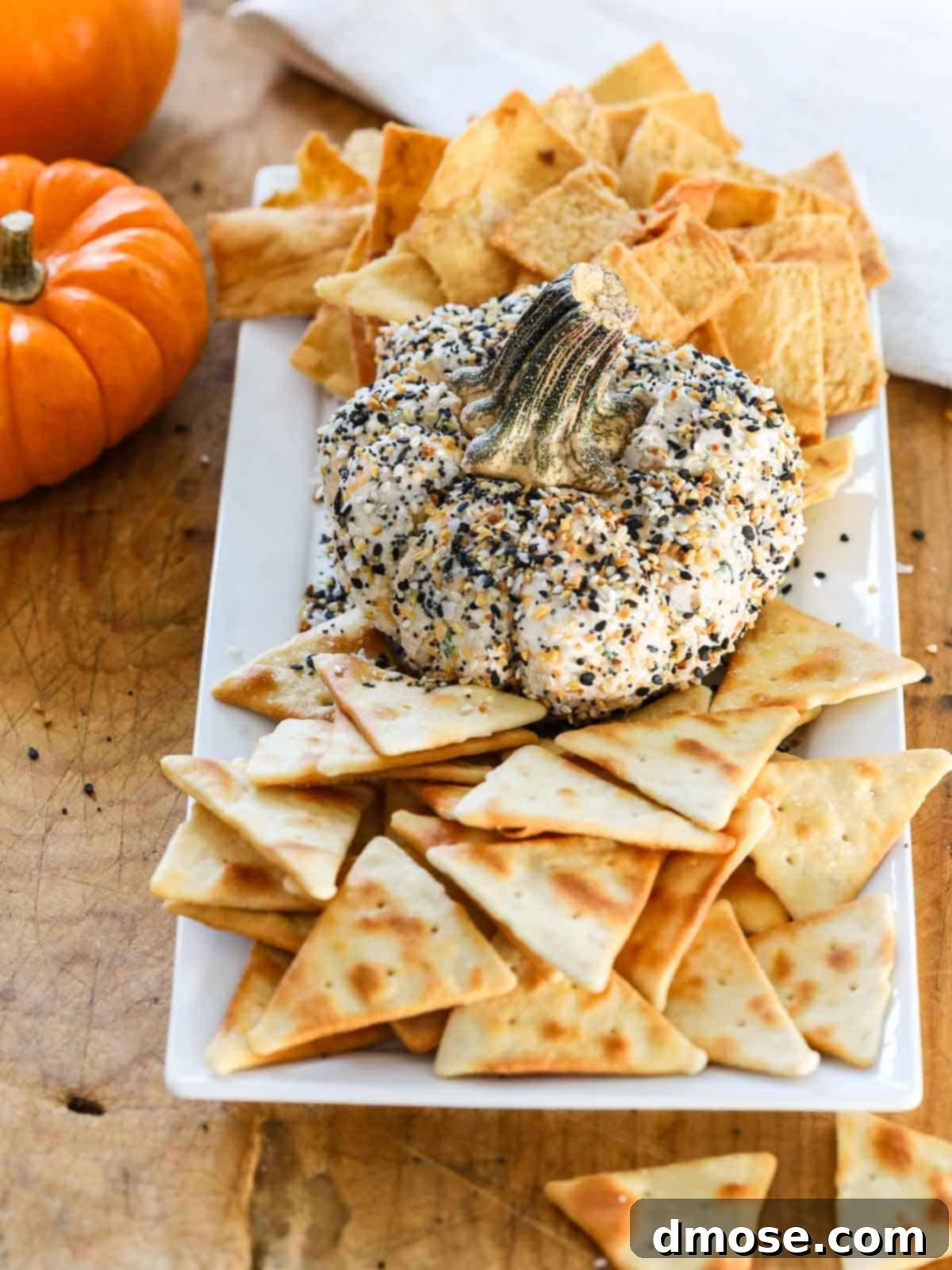Harvest Everything Bagel Pumpkin Cheese Ball 2 Pumpkin-shaped Everything Bagel Cheese Ball on a serving platter with crackers and pita chips.