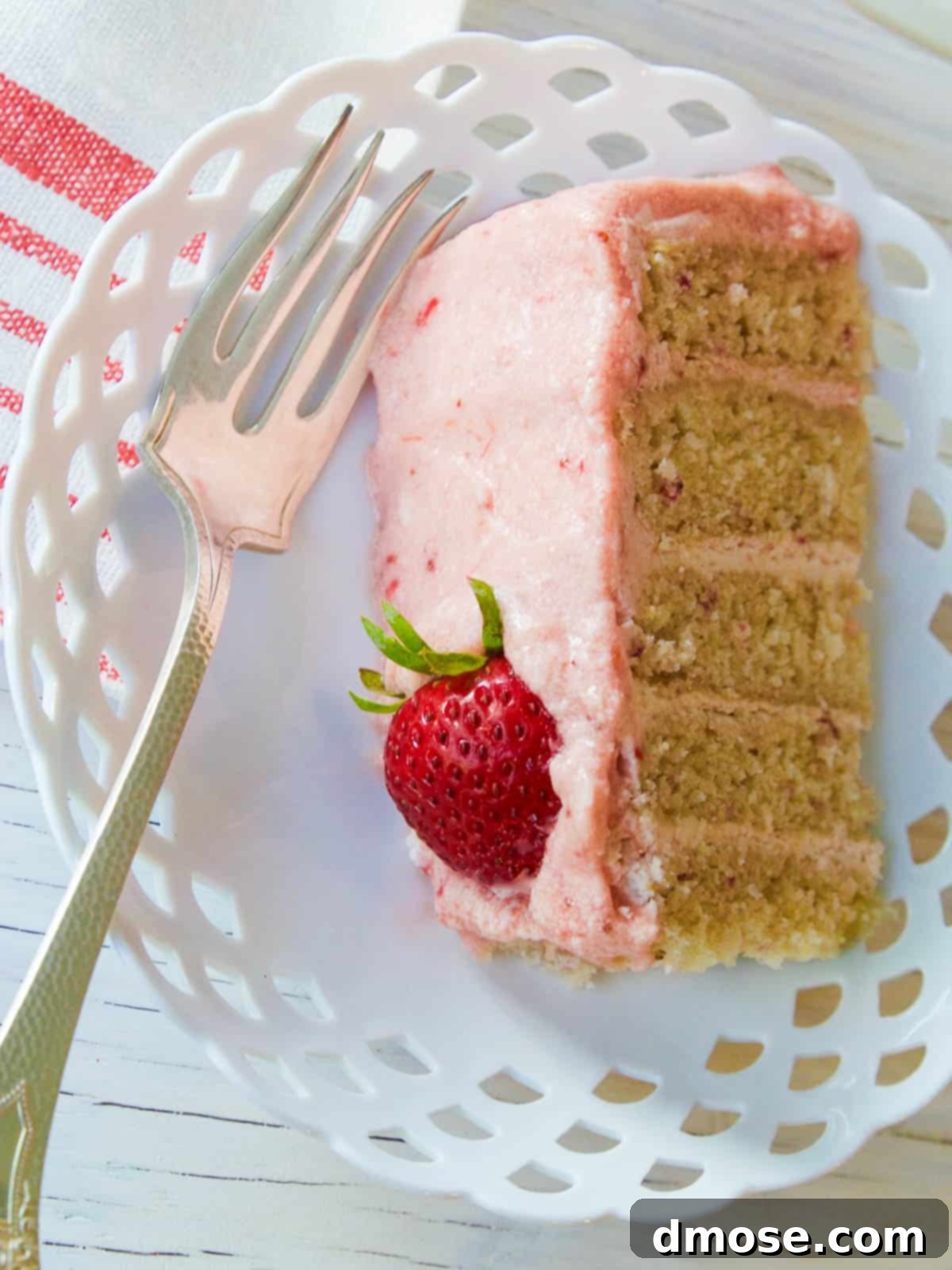 A slice of strawberry cake on a white plate, adorned with a fresh strawberry.