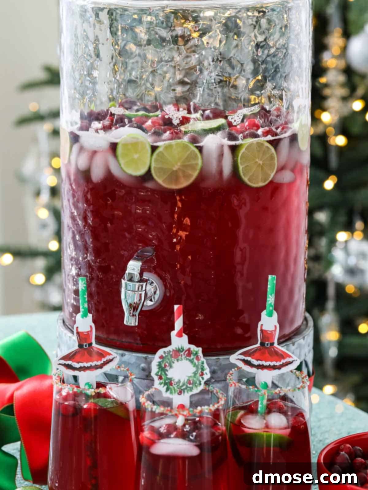 Three elegant glasses filled with Christmas Punch, garnished with cranberries and lime, set against a festive background.