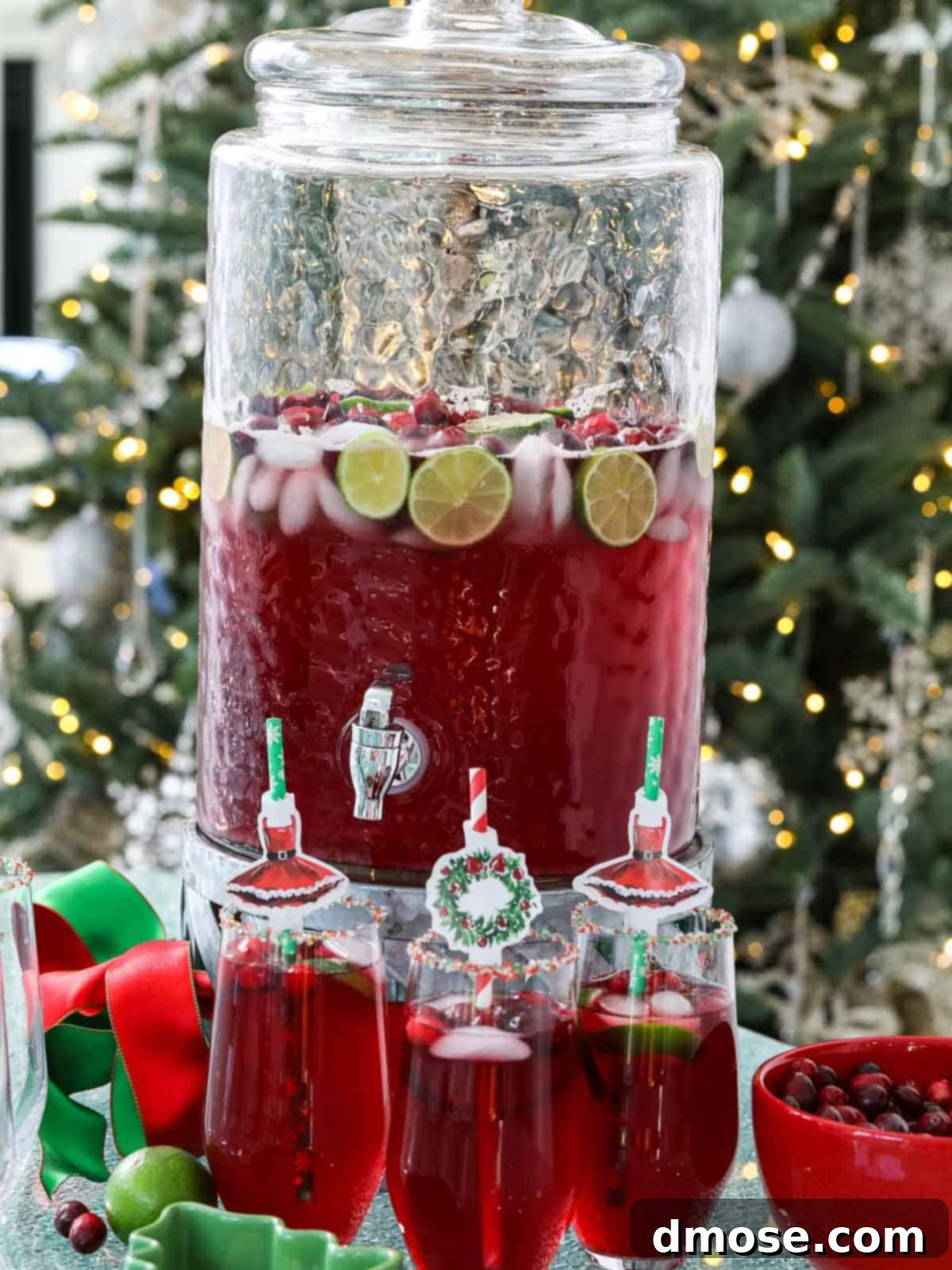 A festive Christmas Punch display with glasses, garnishes, and a subtly blurred Christmas tree in the background.