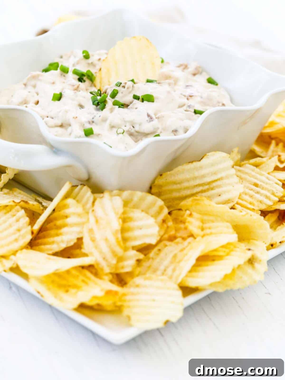 A white dish with French Onion Dip and a ruffled potato chip dipped in it.