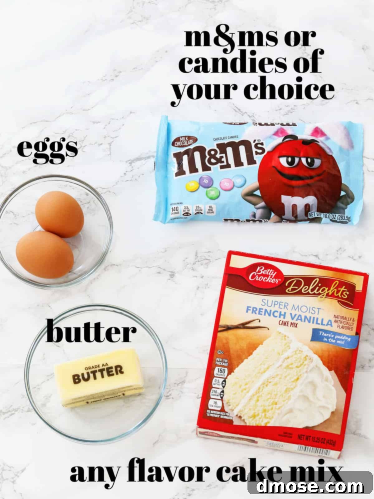 The four simple ingredients for cake mix cookies: a box of cake mix, melted butter, two eggs, and M&Ms, laid out on a white surface.