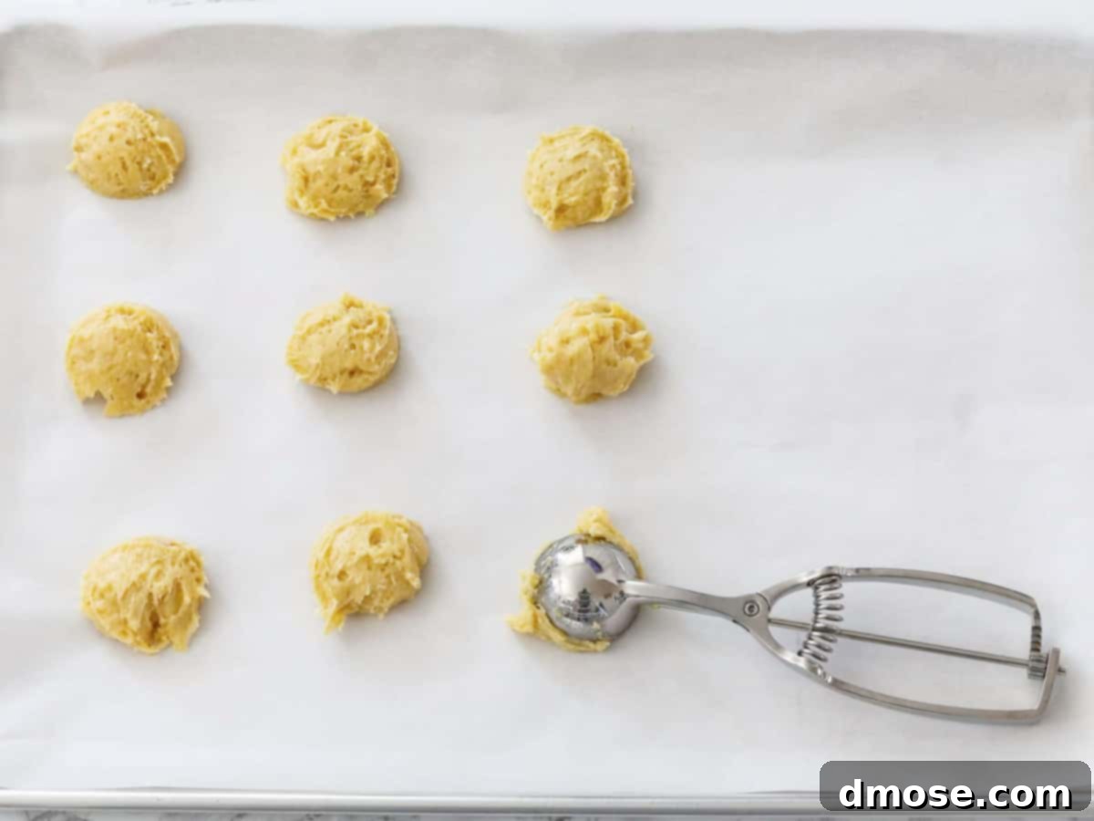 Close-up of cookie dough being scooped onto a parchment-lined baking sheet, showing the consistency of the cake mix cookie dough.
