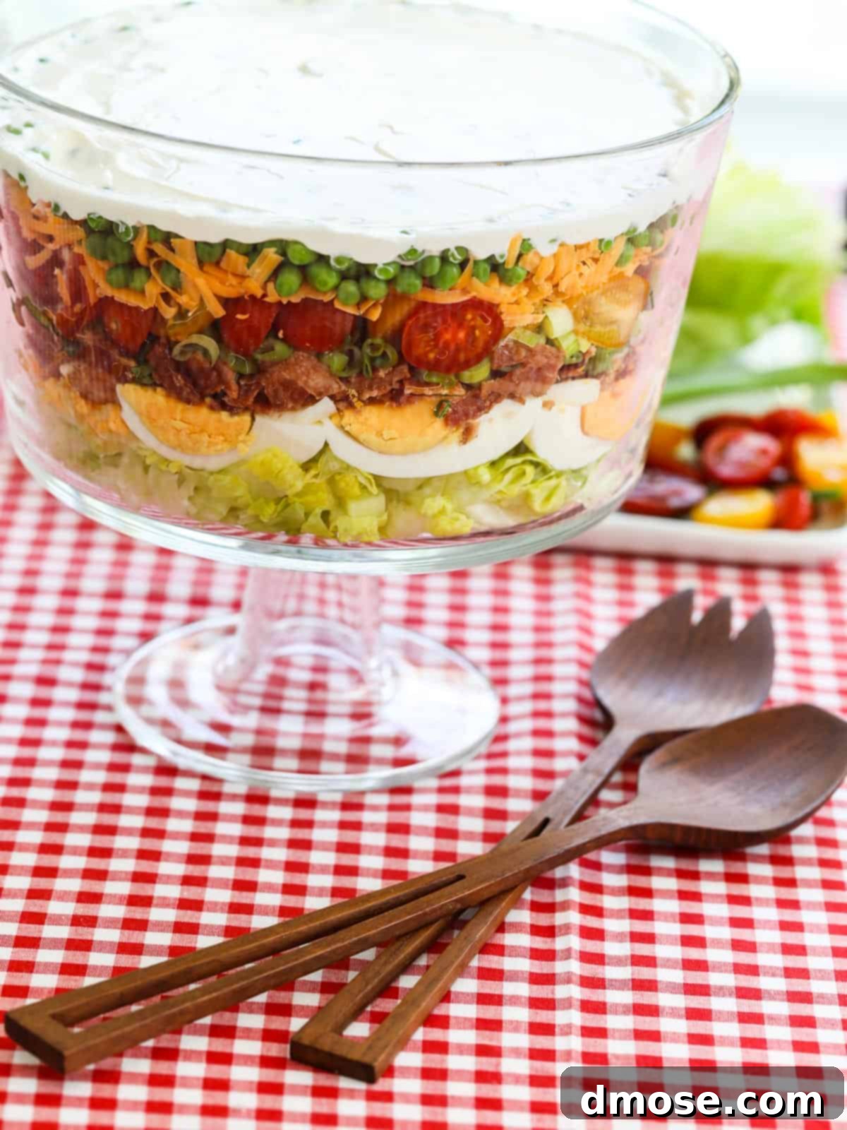 A vibrant seven-layer salad in a large glass trifle bowl, showcasing distinct layers of fresh ingredients.