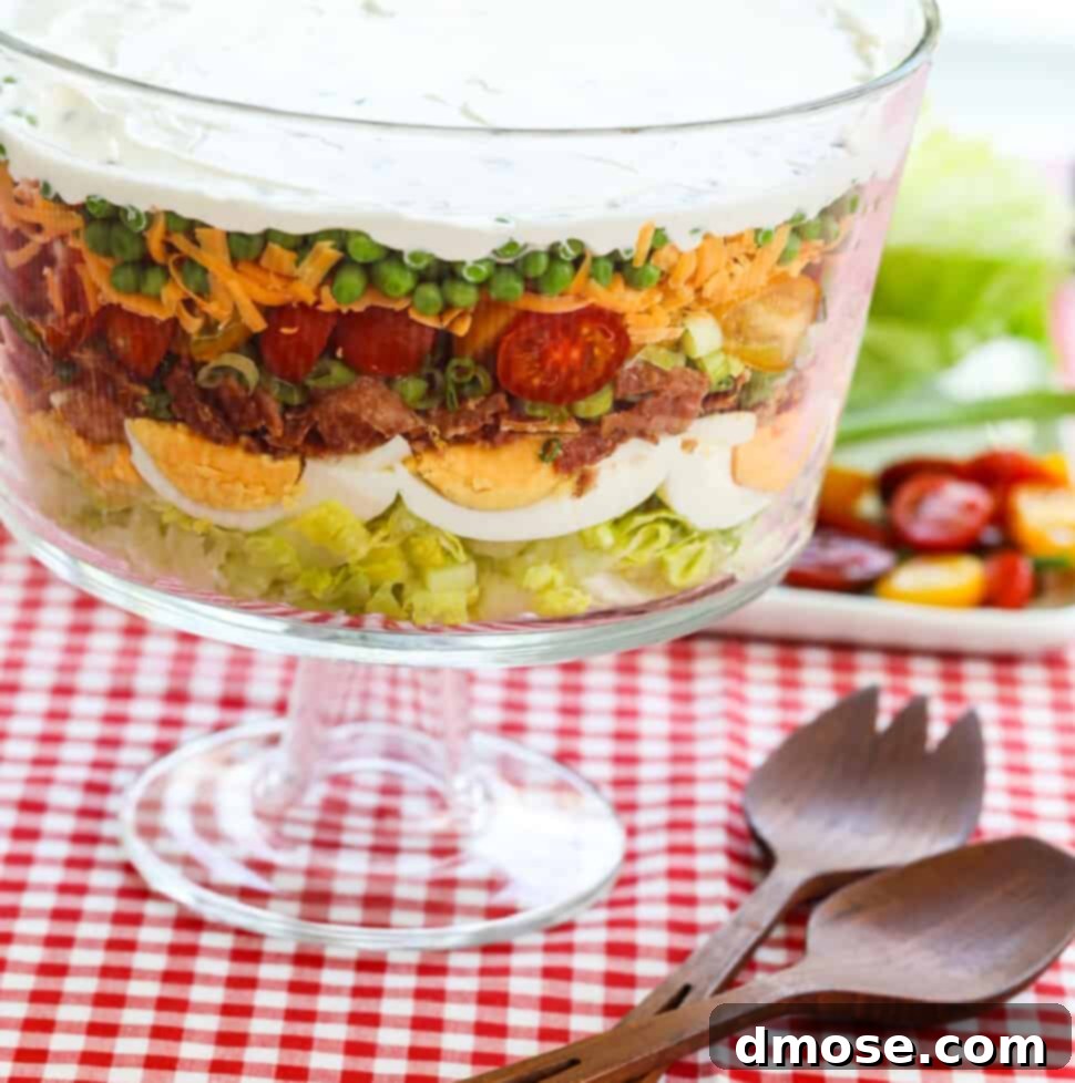 A glass trifle dish filled with 7 Layer Salad full of colorful ingredients.