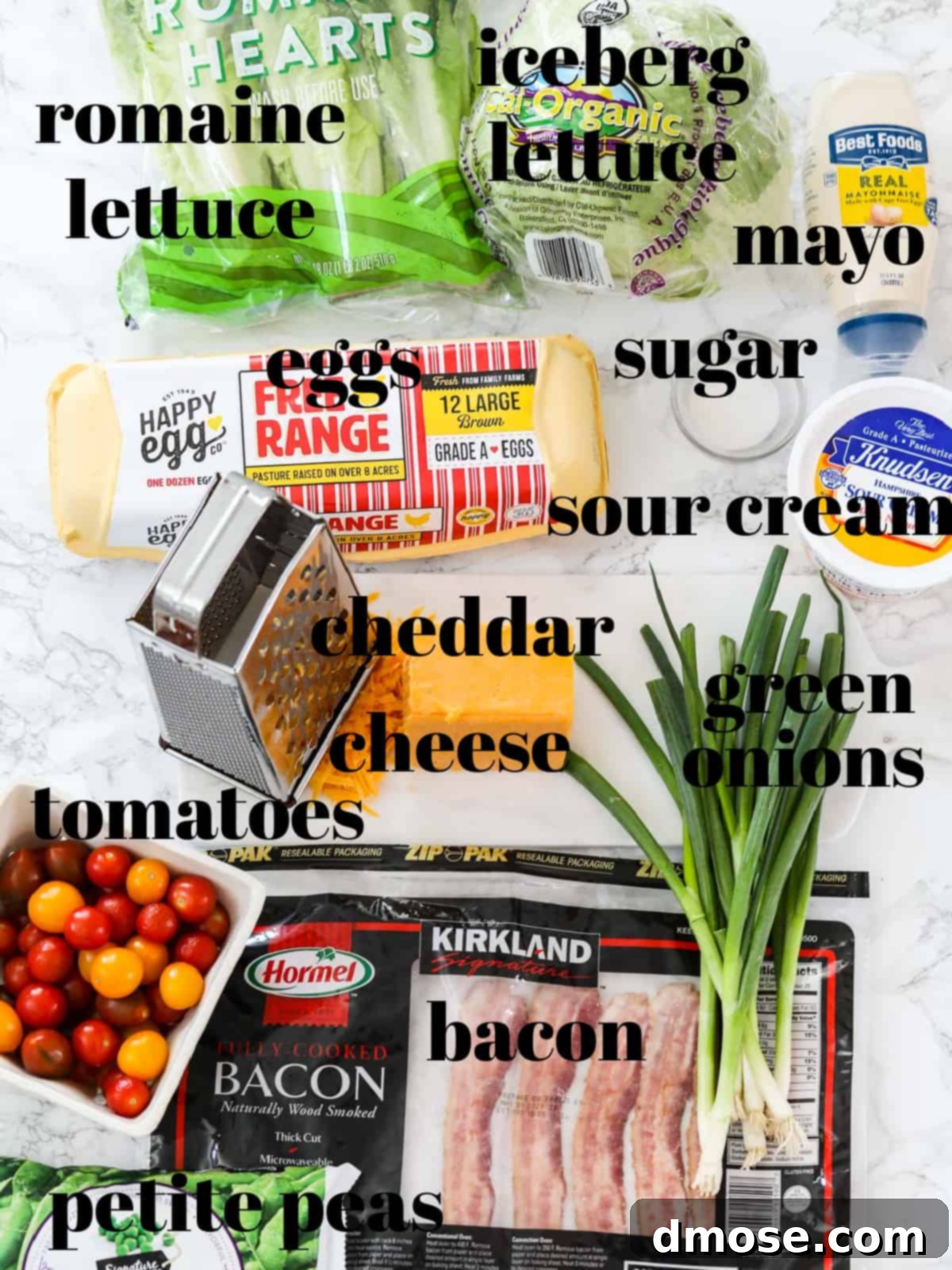 A selection of fresh ingredients laid out for a seven-layer salad, including lettuce, eggs, bacon, tomatoes, and peas.