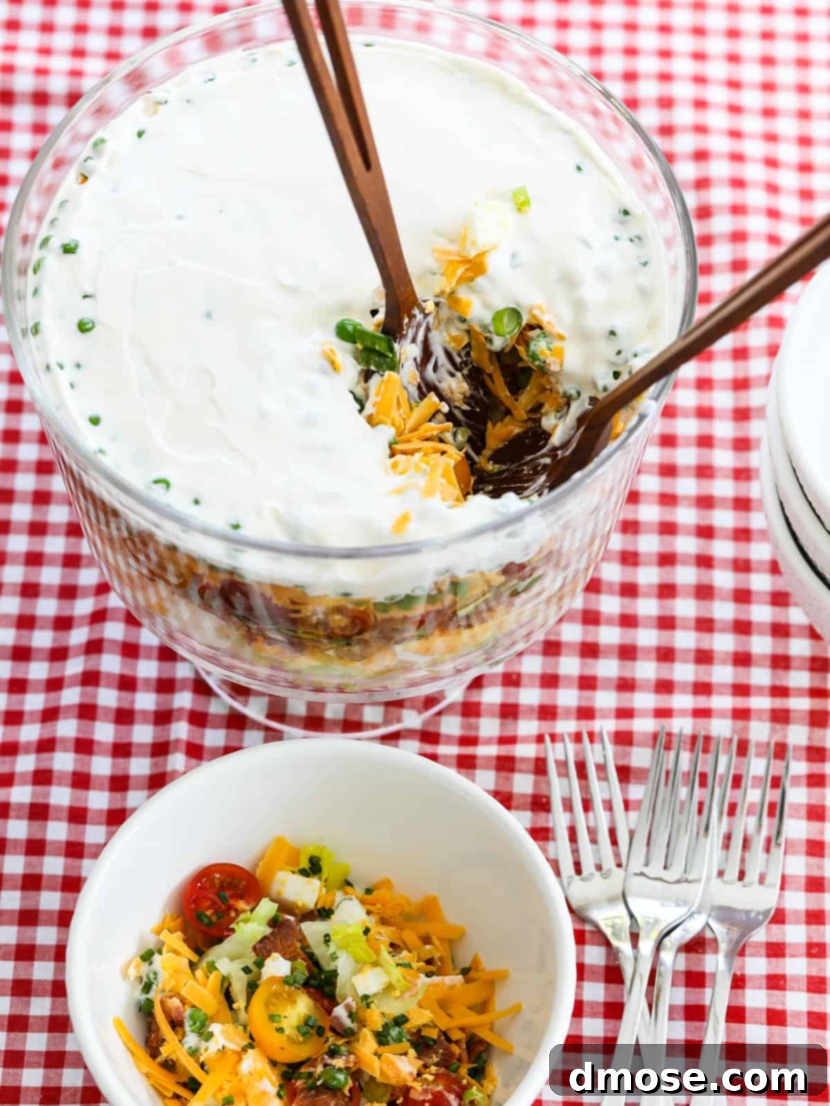 A server scooping 7 Layer Salad from a large bowl into individual smaller bowls.