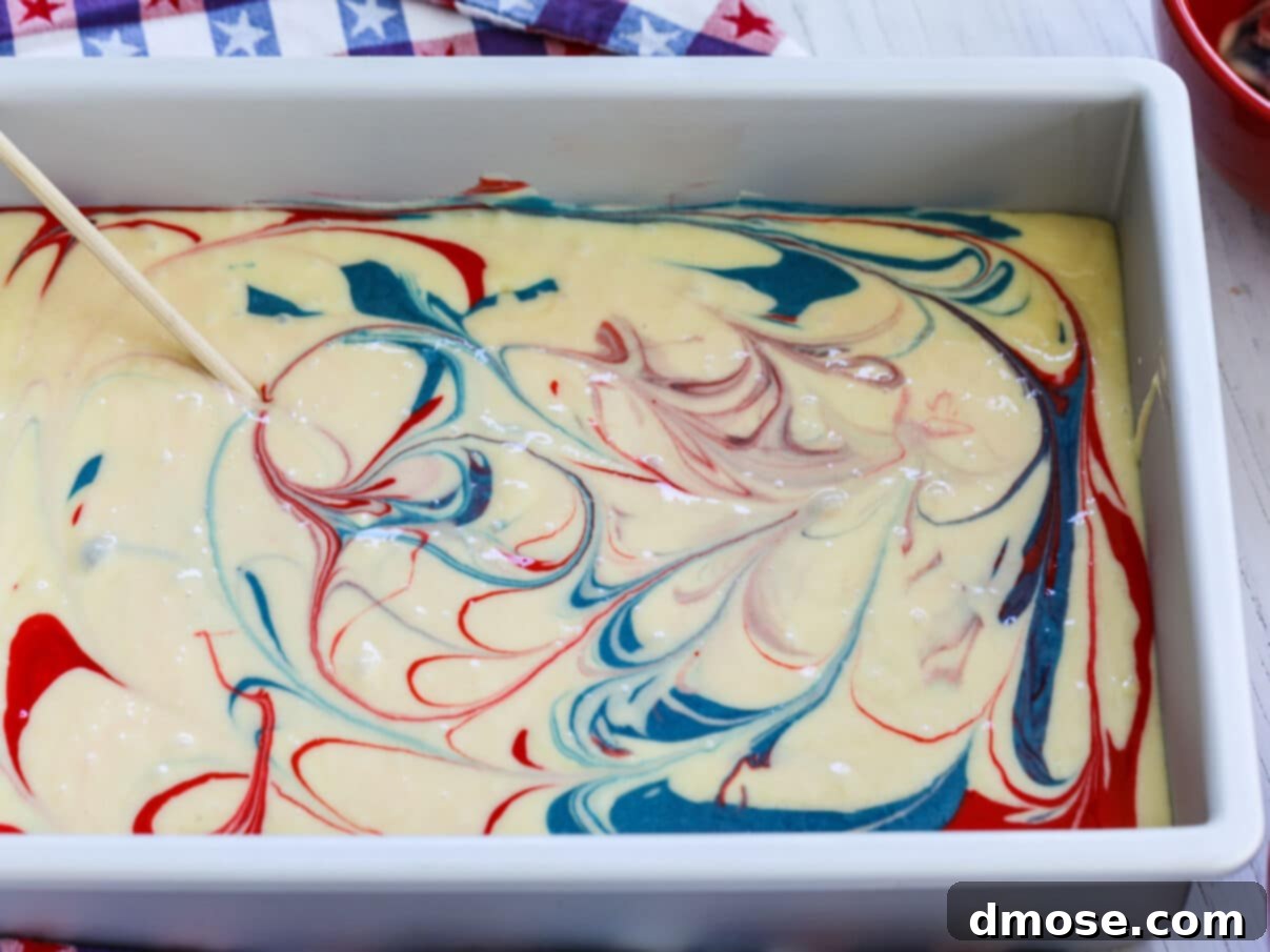 A skewer being used to swirl red, white, and blue cake batter in a pan for an American Flag design.
