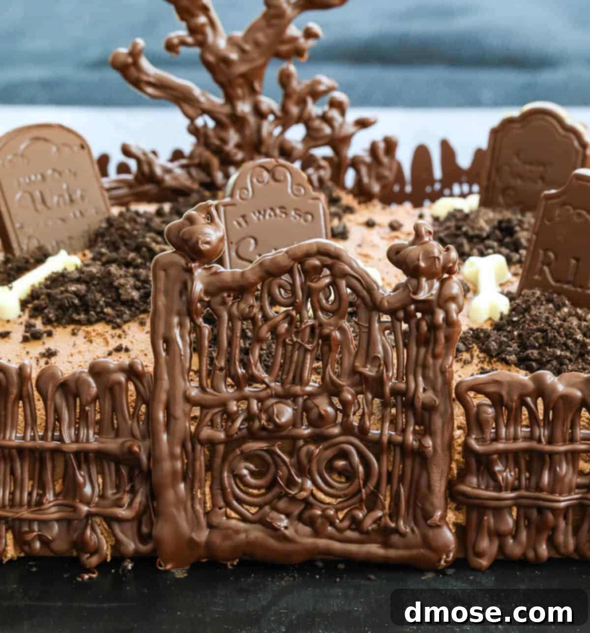Haunted Halloween Cake Delights 2 A beautifully decorated Halloween cake featuring an edible chocolate graveyard scene, including fences, tombstones, a spooky tree, and crushed cookie 'dirt'.