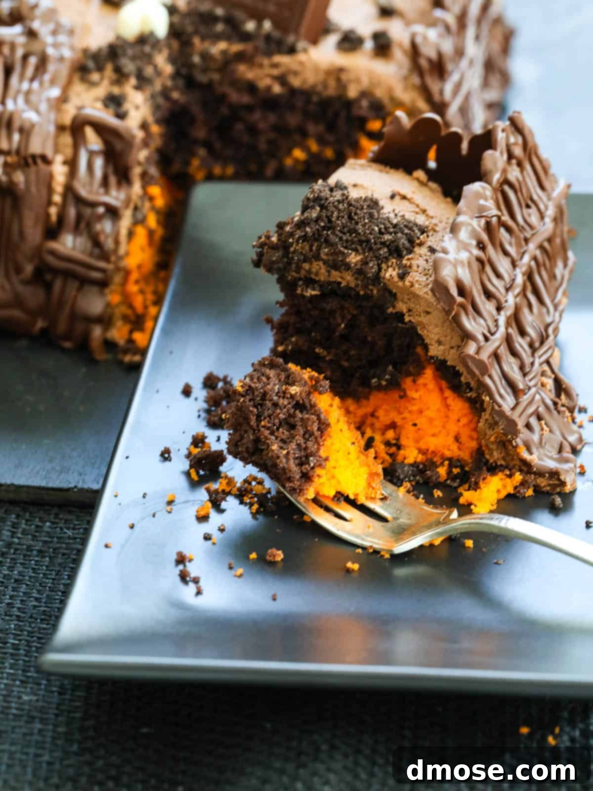 Haunted Halloween Cake Delights 12 A perfectly sliced piece of orange and chocolate marbled Halloween cake, elegantly presented on a black plate with a fork beside it.