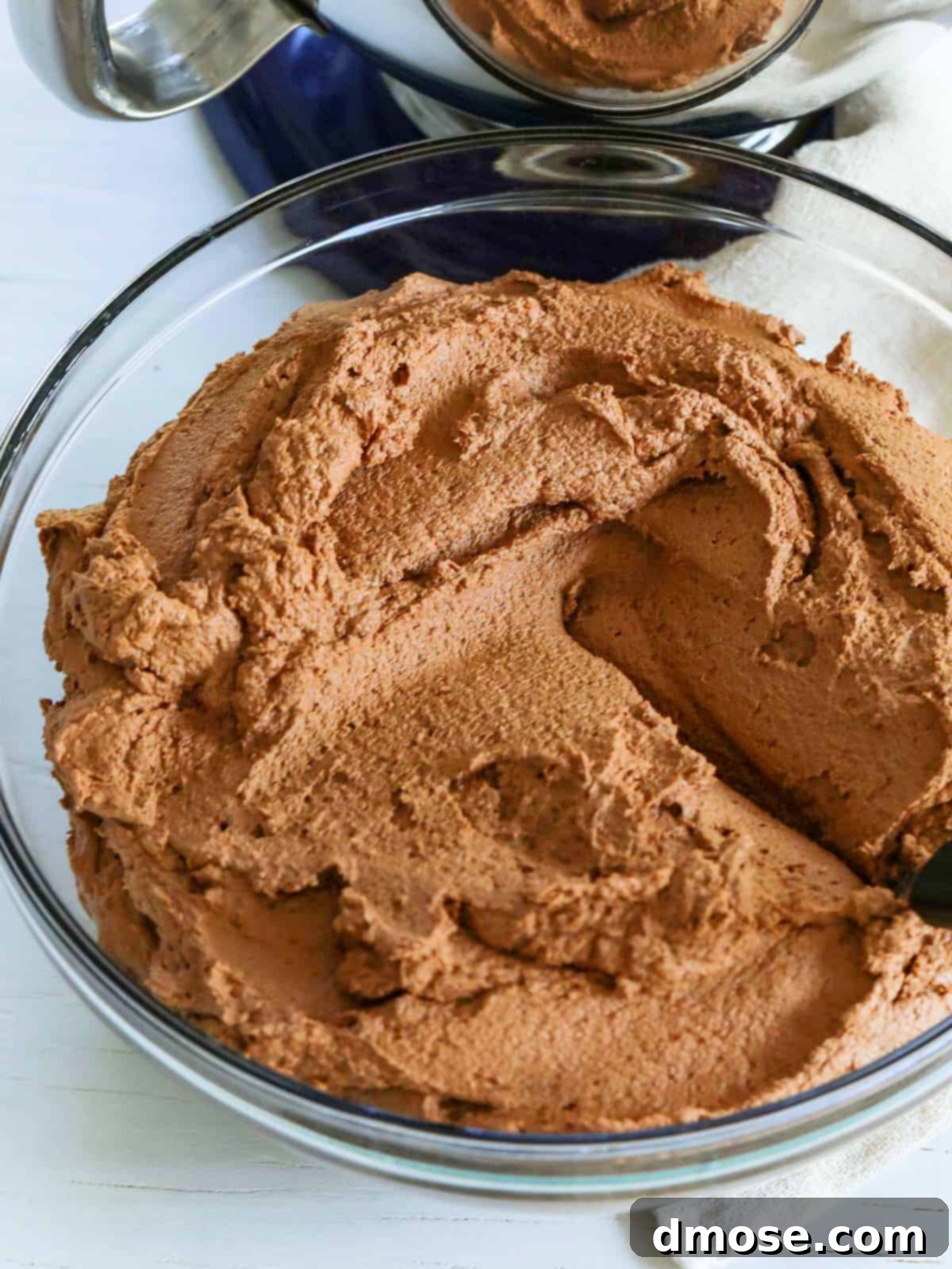 Haunted Halloween Cake Delights 5 A large glass bowl full of rich chocolate frosting with a small offset spatula resting in it, ready to be used for frosting a cake or cupcakes.