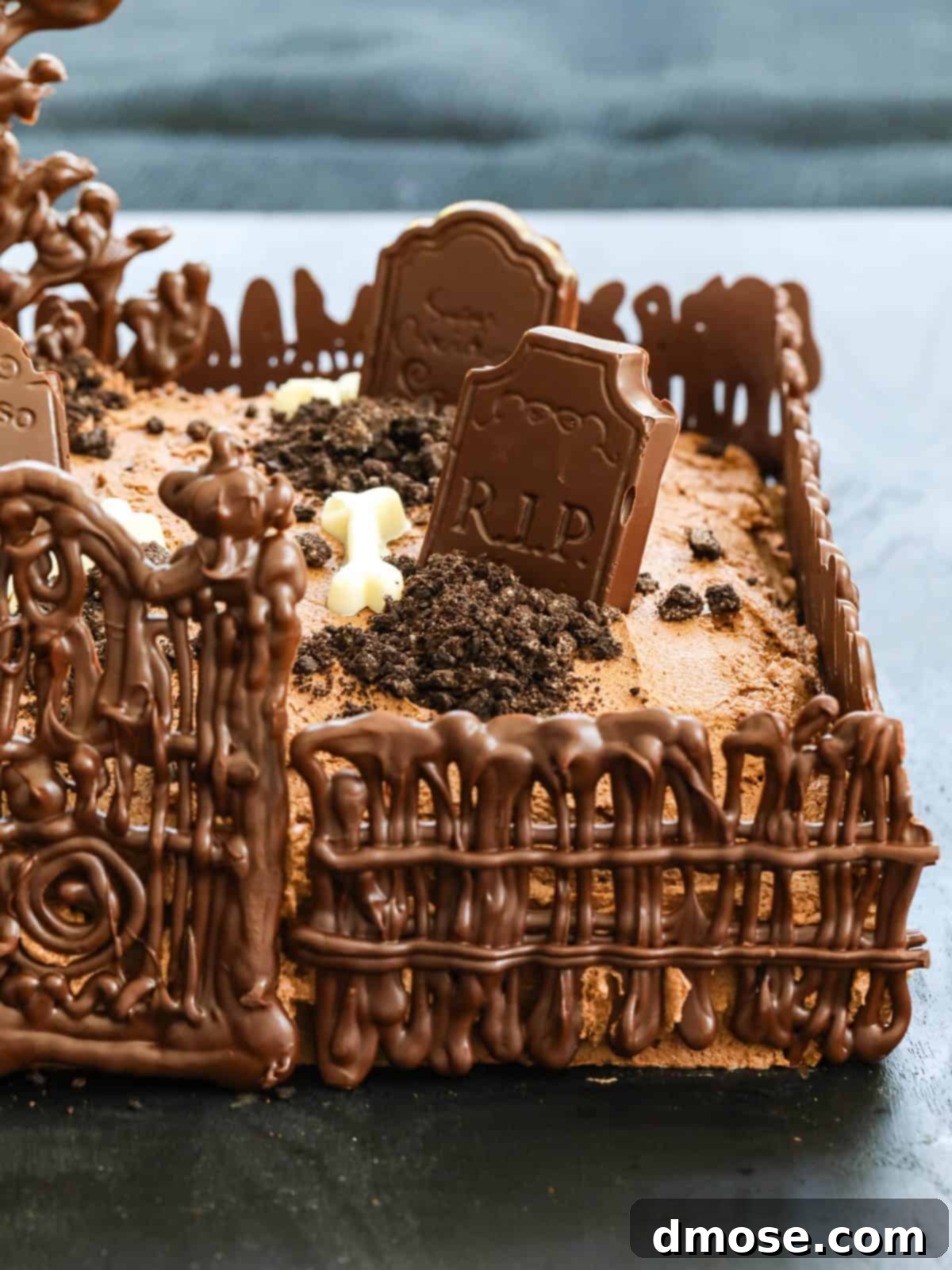 Haunted Halloween Cake Delights 7 Close-up of the Halloween Graveyard Cake with chocolate decorations like fences and tombstones placed on top, with crushed Oreos for 'dirt'.
