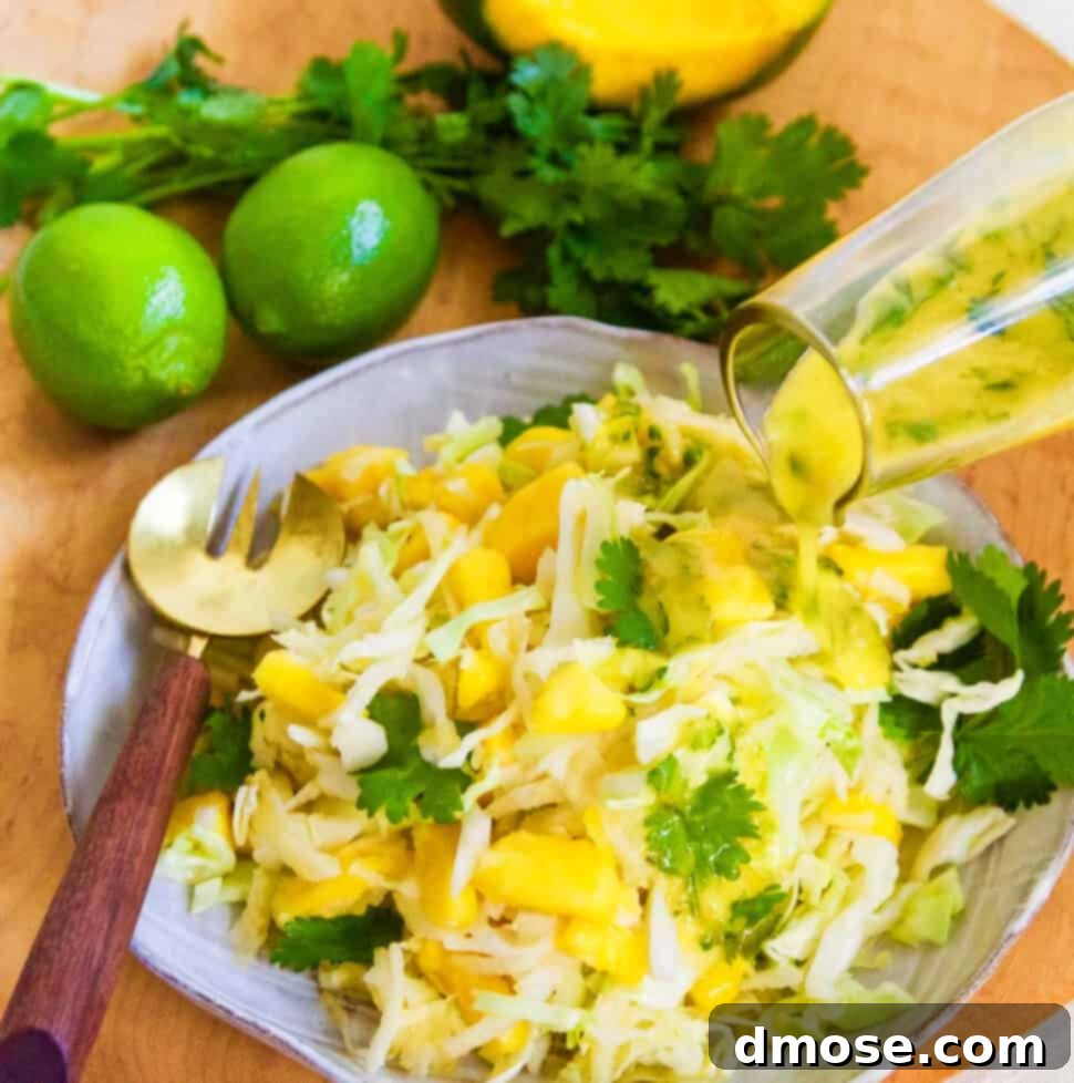 Pouring dressing on a full plate of mango slaw with a gold fork on edge of ceramic plate.
