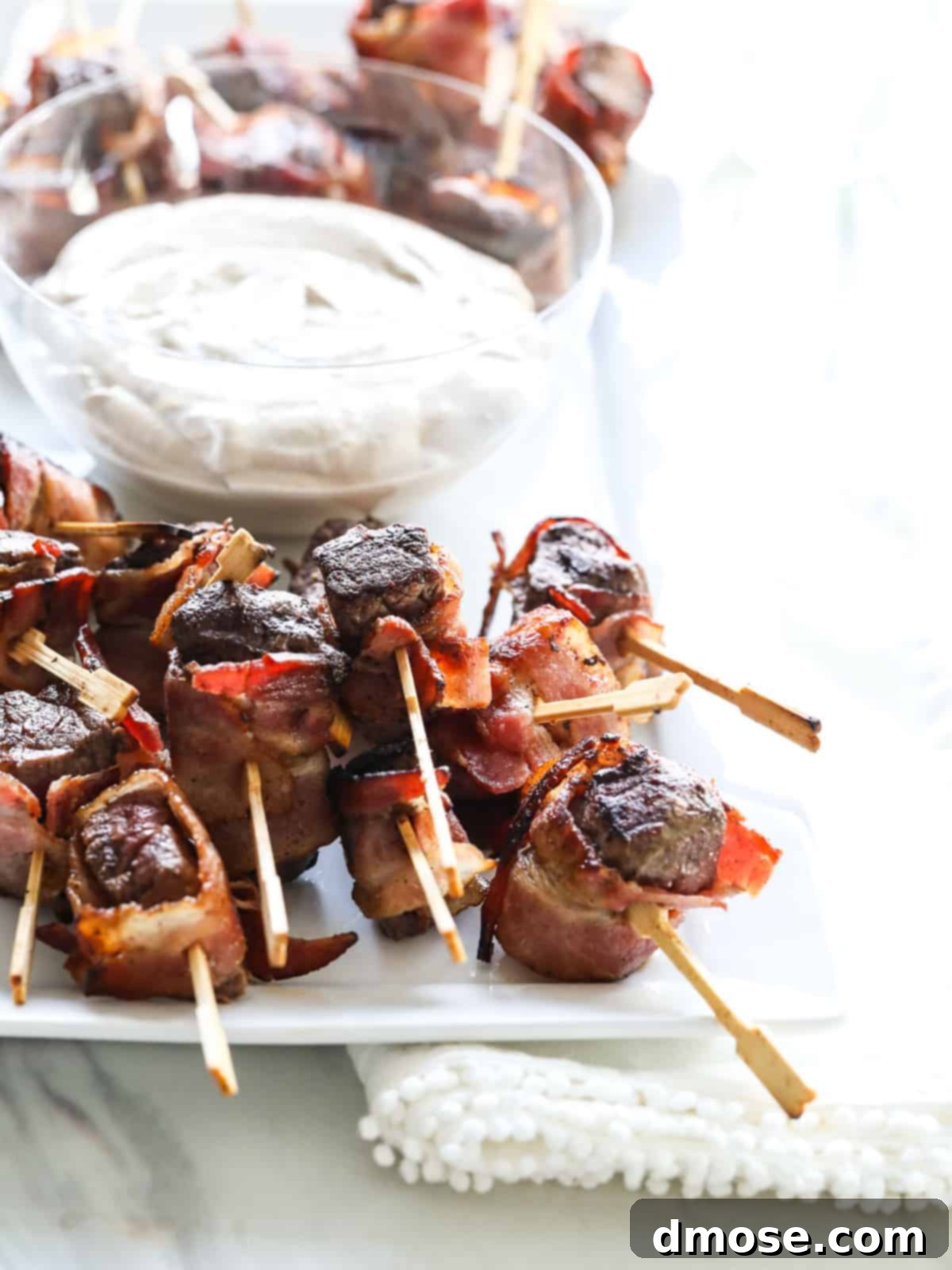 Close-up of a bacon-wrapped filet mignon bite with a dollop of horseradish sauce.