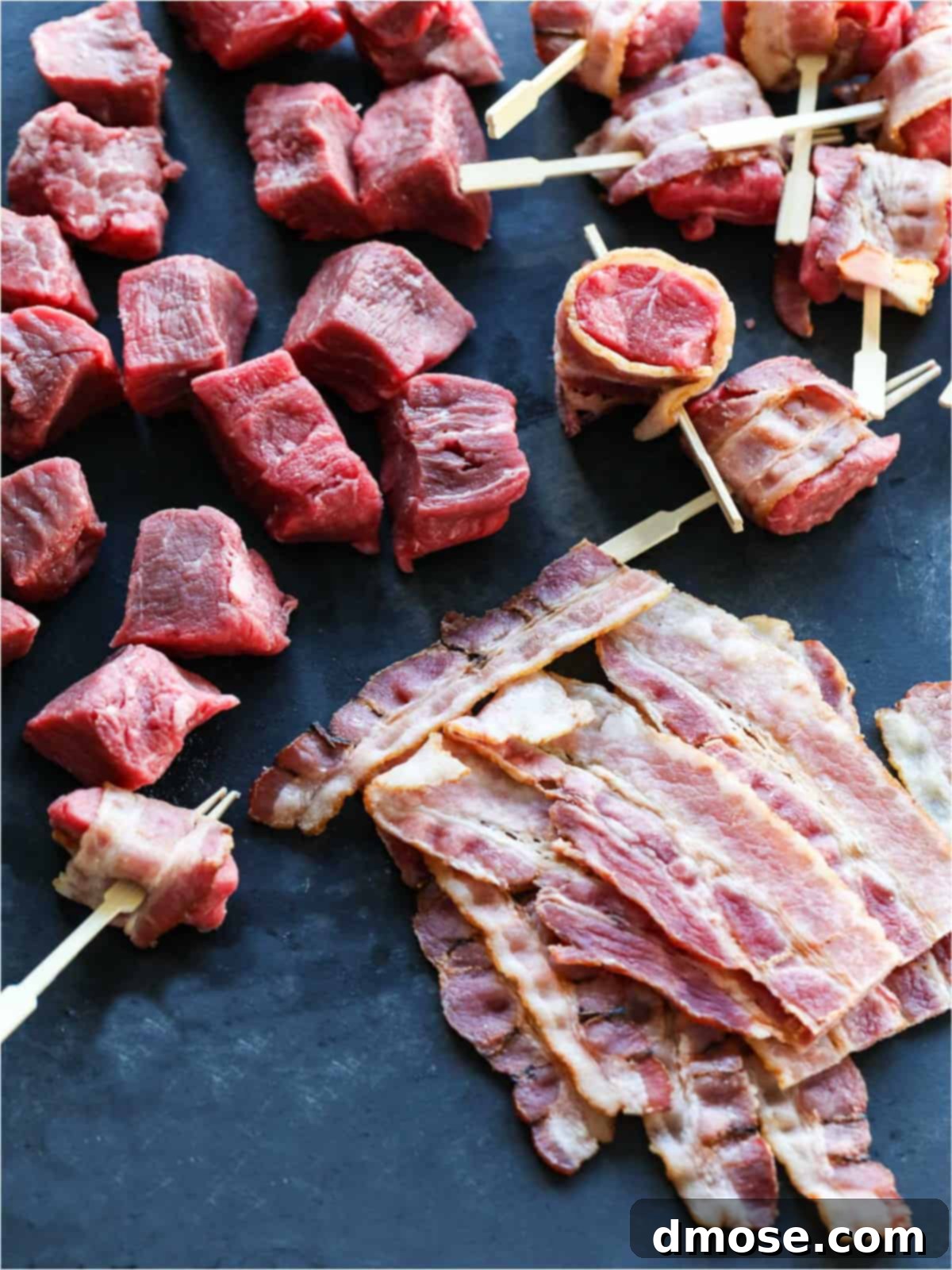 Process shot of bacon being wrapped around pieces of filet mignon and secured with toothpicks.