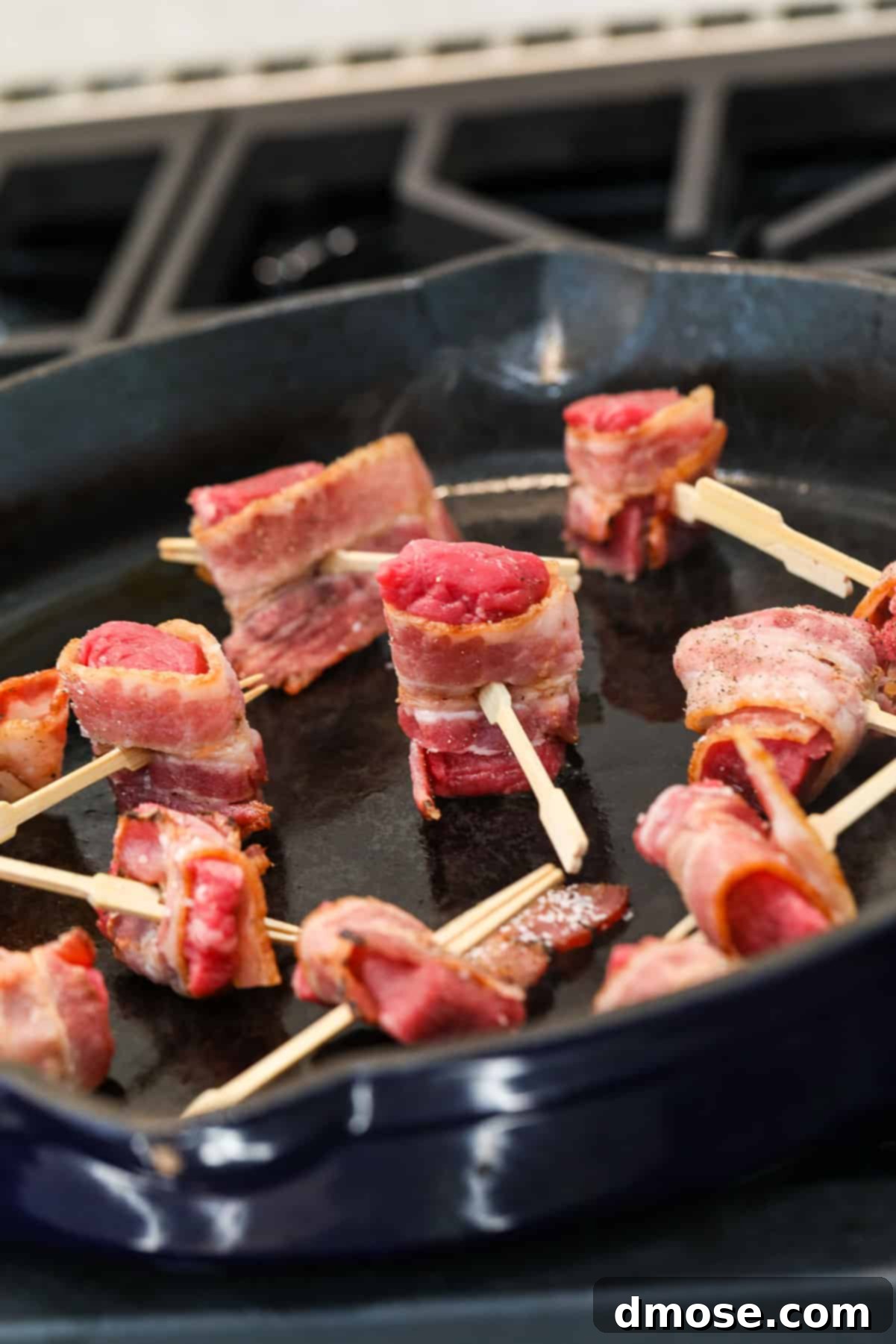 Bacon-wrapped filet mignon pieces searing in a hot skillet.