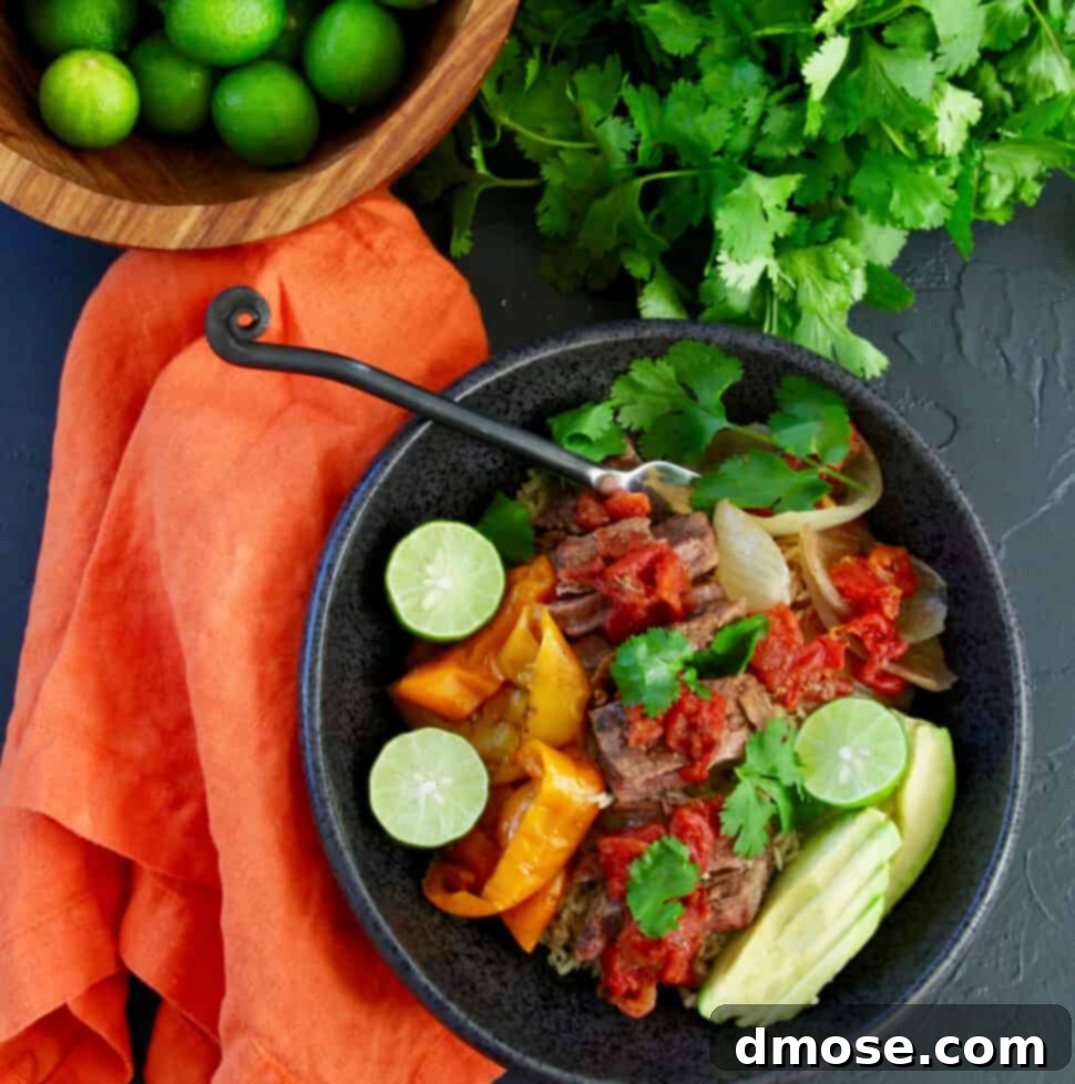 Slow Cooker Fall Apart Beef 8 A table with a black bowl filled with shredded beef on rice with onions and bell peppers garnished with limes, avocado, and cilantro.