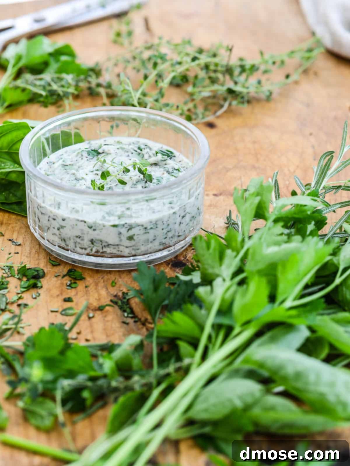 Herb butter in a small glass container on a cutting board with herbs.