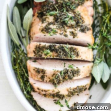 Top down view of a roasted turkey breast sliced thick and garnished with fresh herbs.