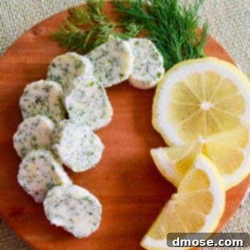 Small brown round cutting board with slices of lemon dill butter garnished with fresh lemon and dill.