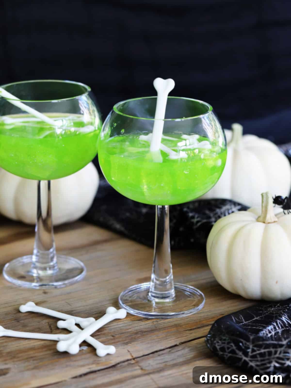 Mystic Melon Elixir 2 Two emerald green Witches Brew Midori Sours, garnished with white plastic bones and surrounded by spooky Halloween decorations, ready for a festive party.