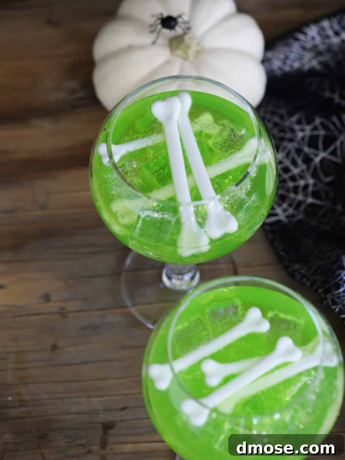 Mystic Melon Elixir 3 A top-down view of two glasses filled with luminous green Midori vodka drinks, elegantly garnished with white plastic bones, perfectly set for a Halloween celebration.