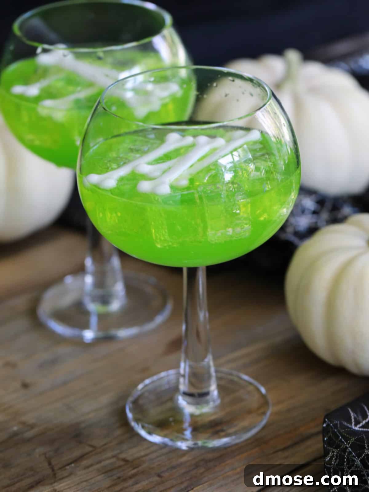 Mystic Melon Elixir 5 Two tall, elegant glasses filled with luminous green Witches Brew Midori Sours, garnished with white plastic bones, perfectly presented for a Halloween party.