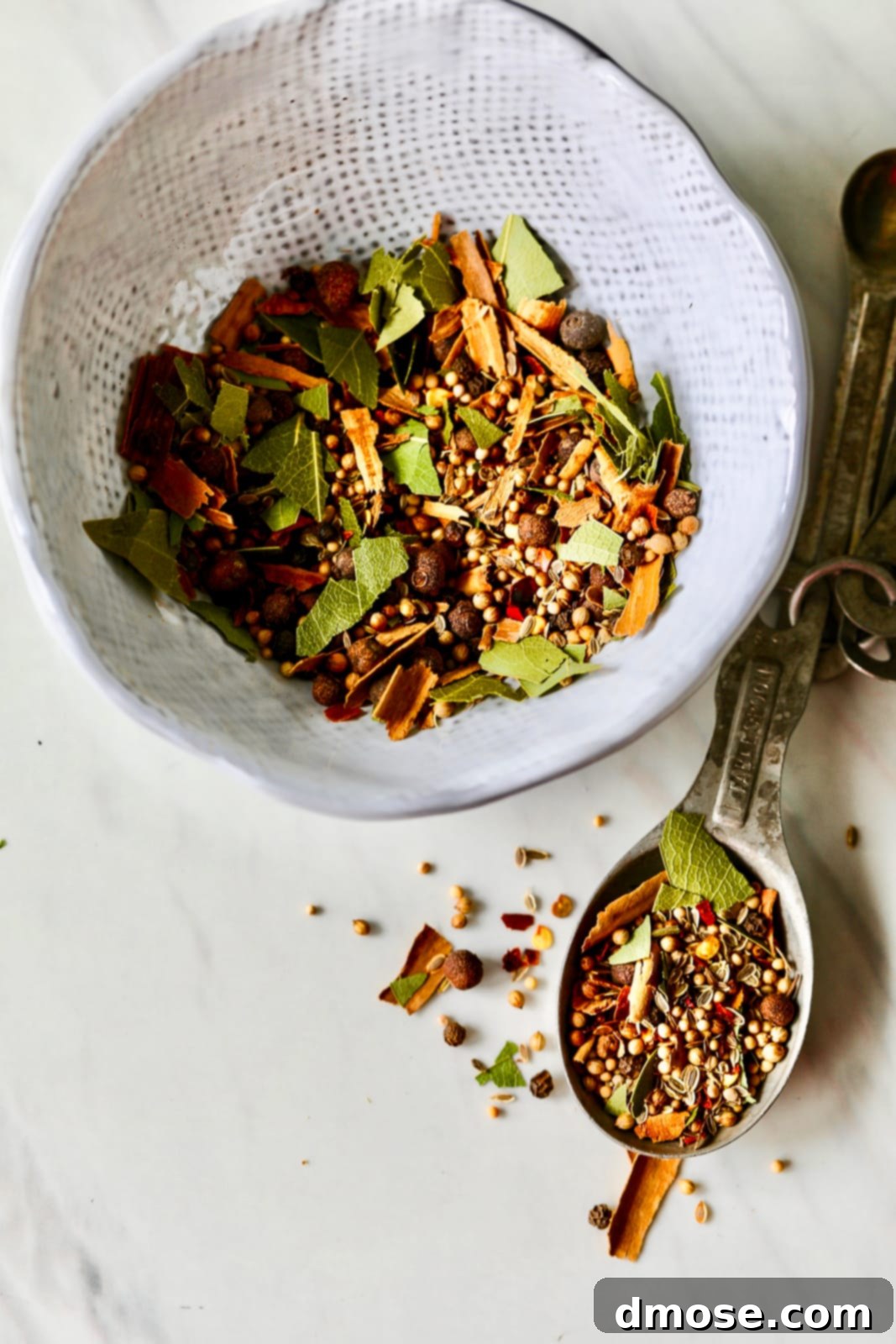 Slow-Cooked Corned Beef Perfection 16 A white ceramic bowl filled with pickling spice and some in a tablespoon on a kitchen counter.