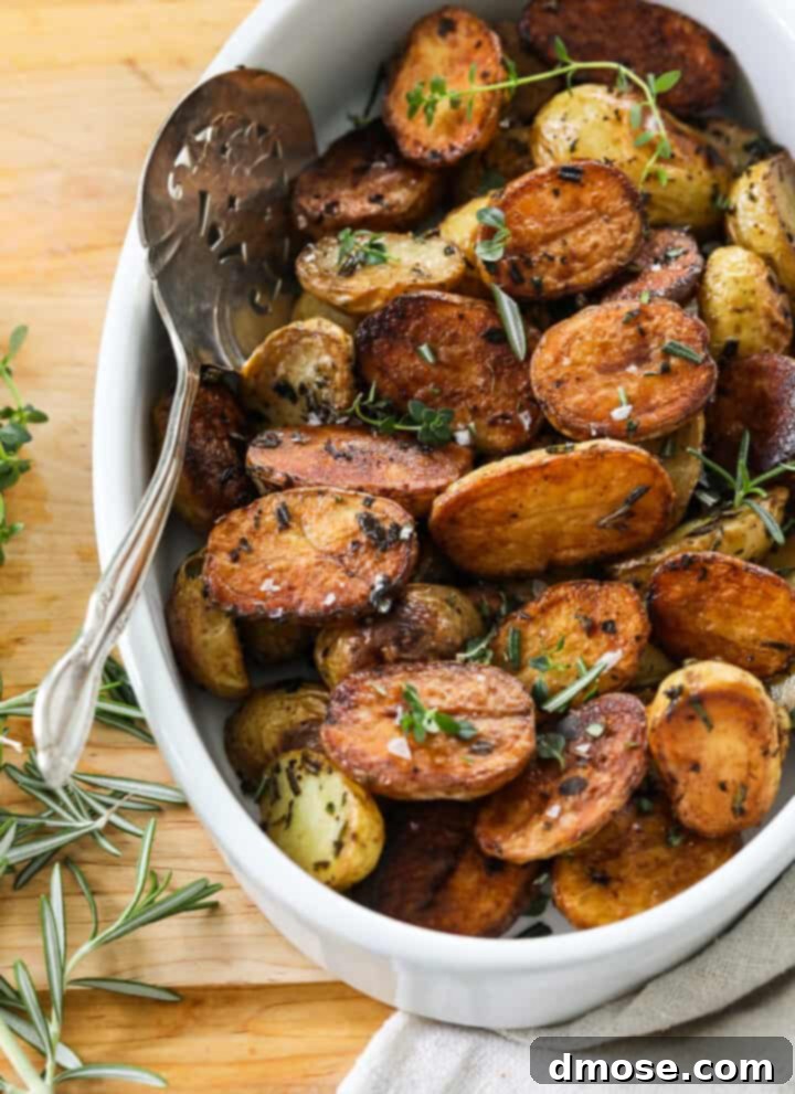 Slow-Cooked Corned Beef Perfection 21 A white oval dish filled with golden brown roasted baby potato halves with a silver serving spoon.