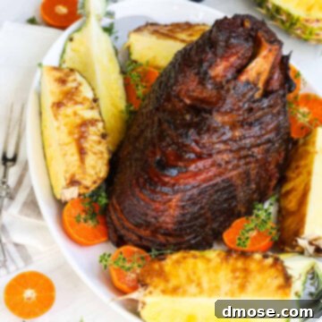 Rich Double Smoked Ham Zesty Orange Honey Glazed 18 A spiral baked ham on white platter with wedges of pineapple and sliced oranges.