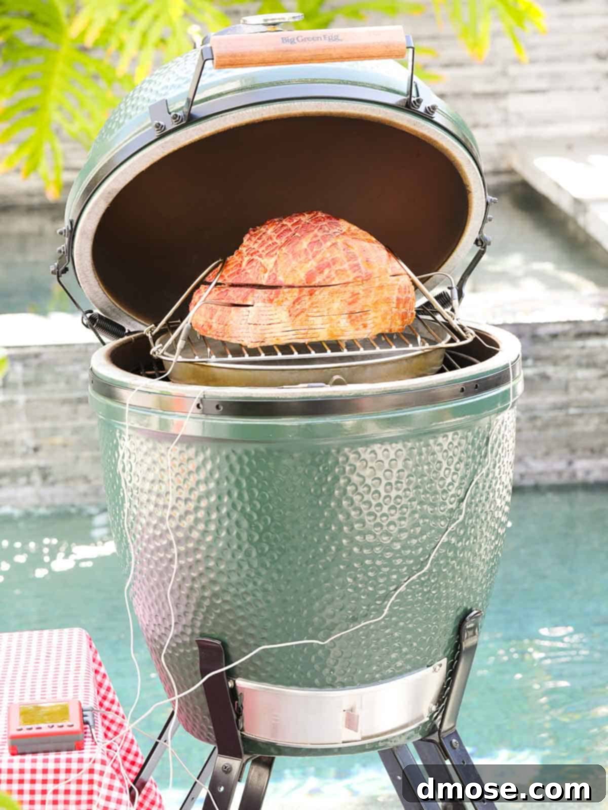 Rich Double Smoked Ham Zesty Orange Honey Glazed 7 A large spiral ham smoking inside a Big Green Egg kamado grill, with a probe thermometer inserted.